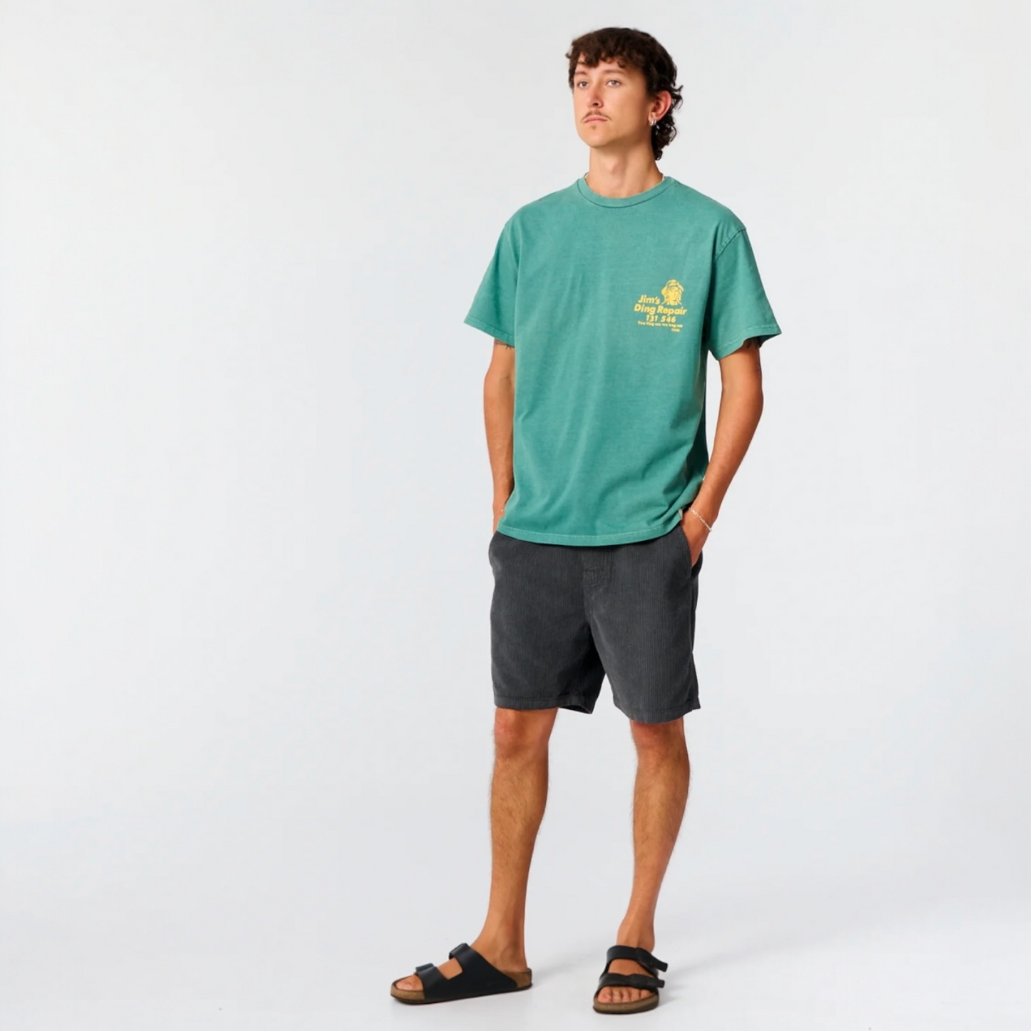 Person wearing a green t-shirt with a logo and dark shorts on a white background