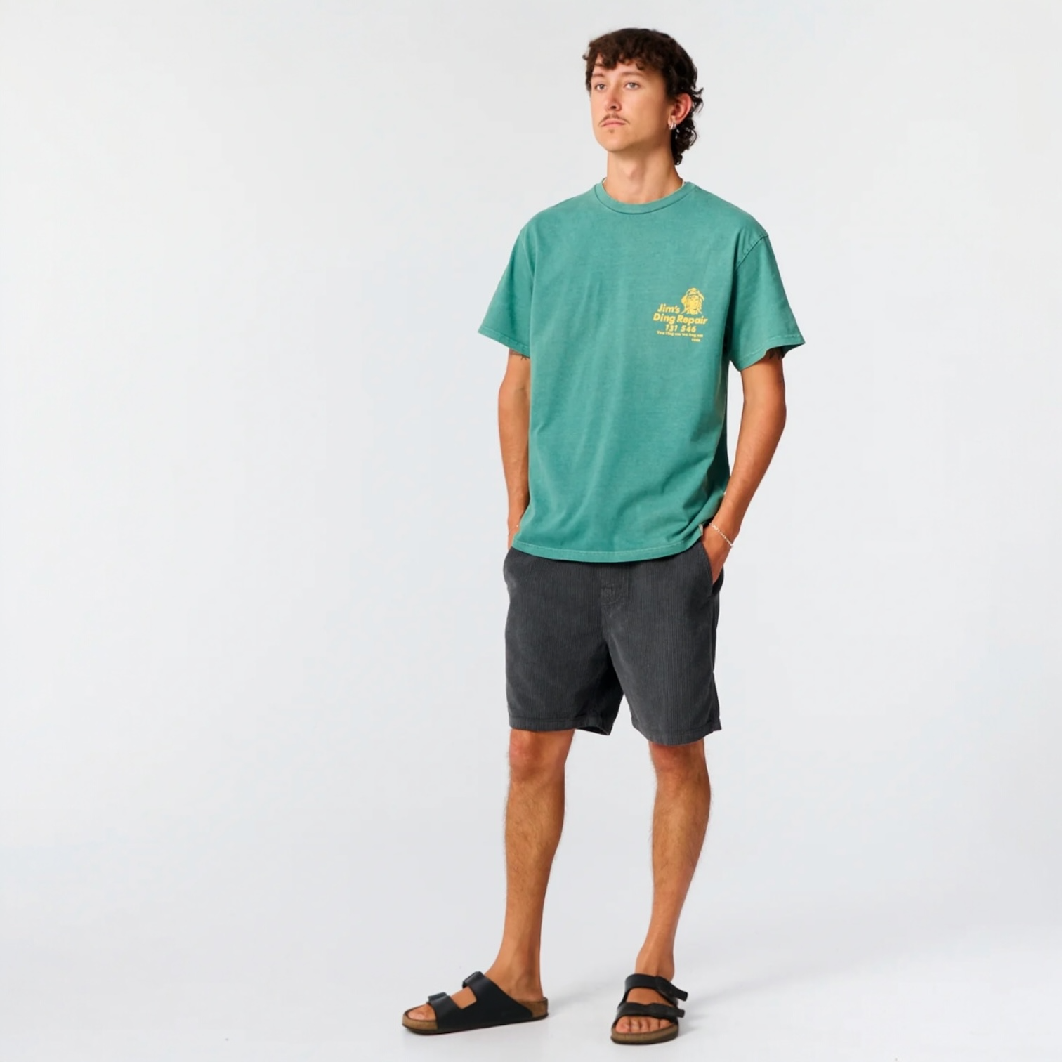 Person wearing a green t-shirt with a logo and dark shorts on a white background