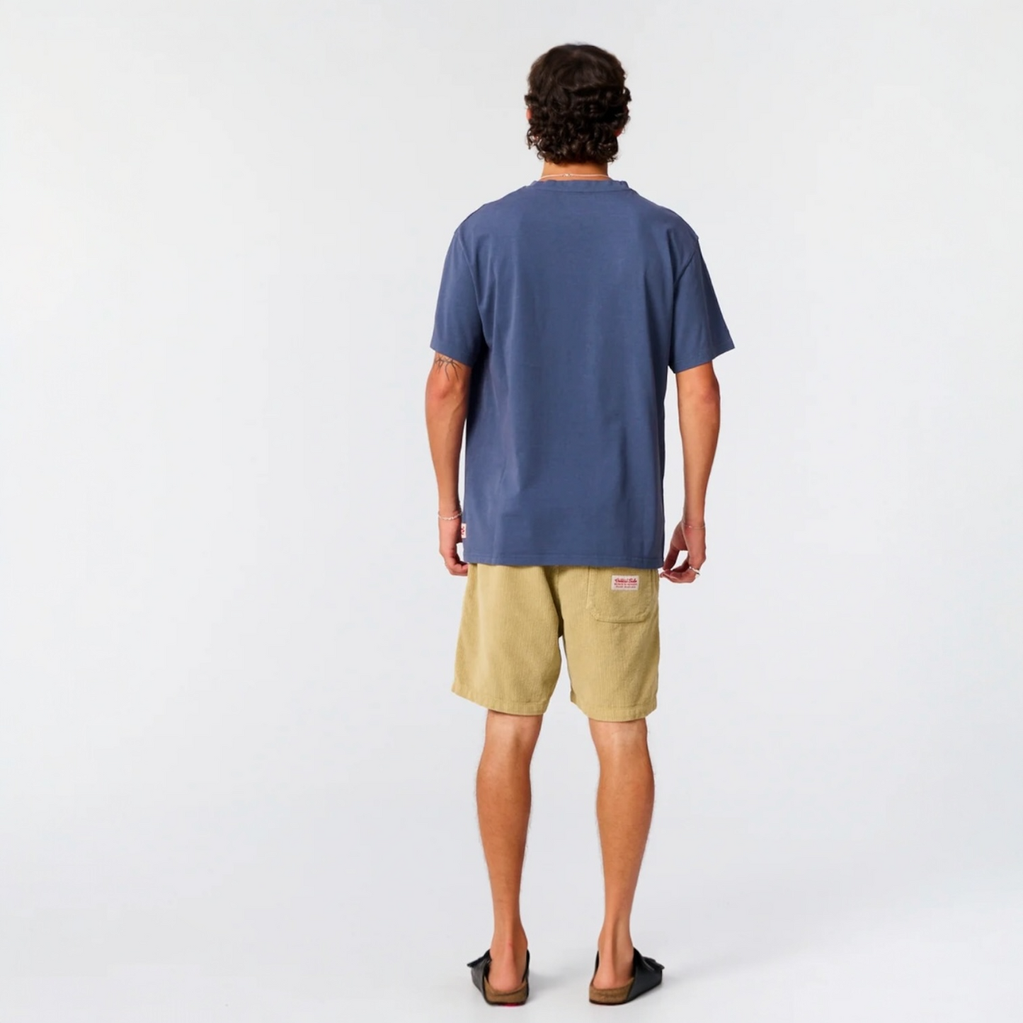 Man wearing a blue t-shirt and beige shorts on a white background