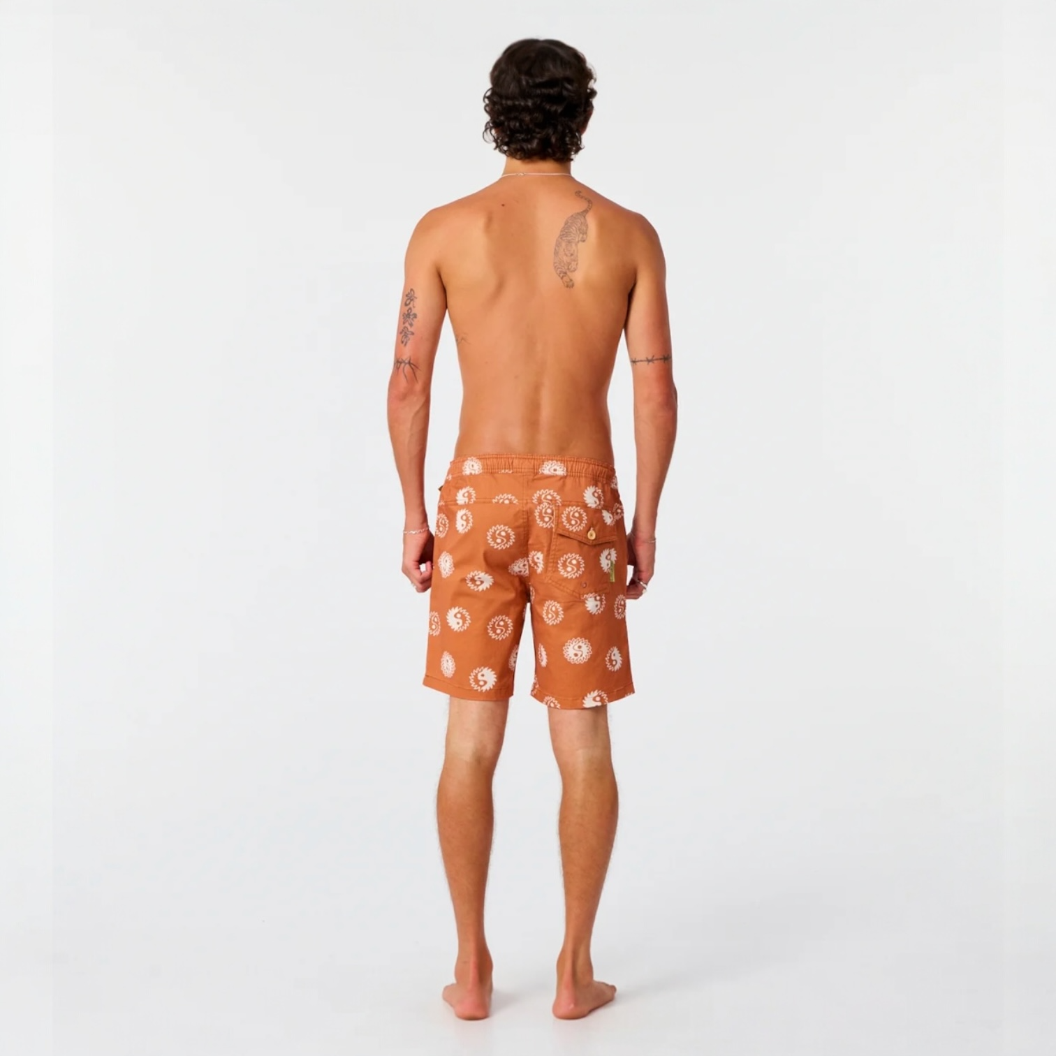 Man wearing orange swim shorts with a pattern on a white background