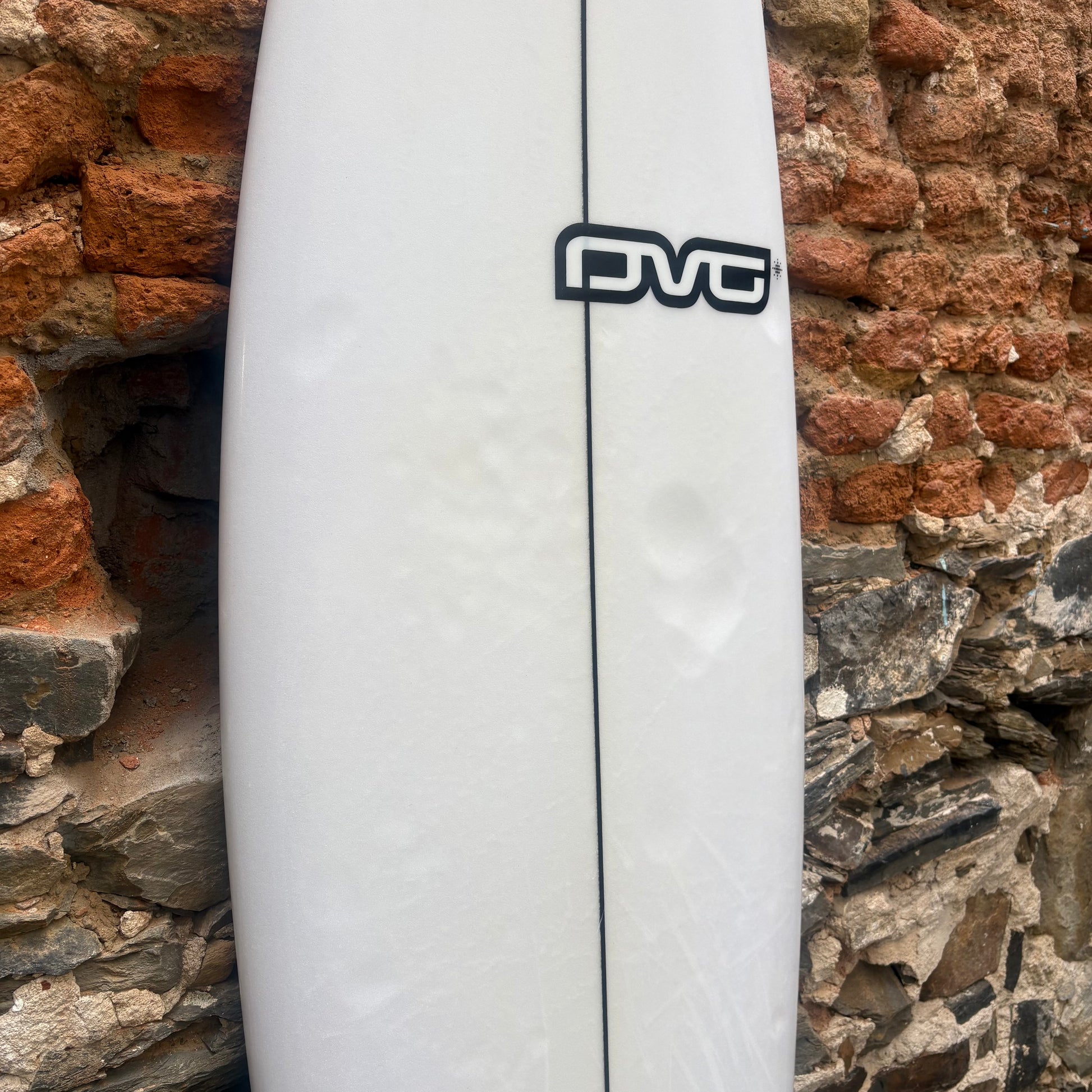 White surfboard with a black logo against a stone wall