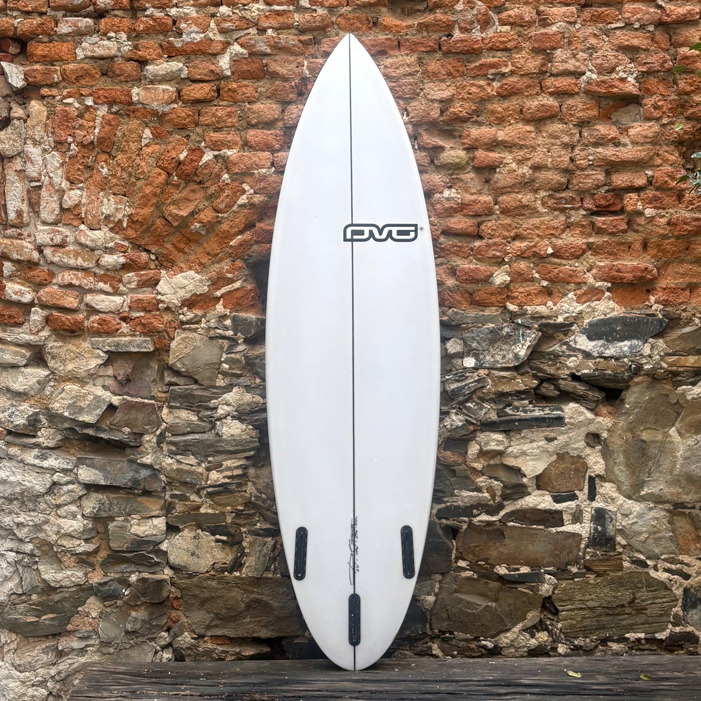 White surfboard with a logo against a rustic stone wall.