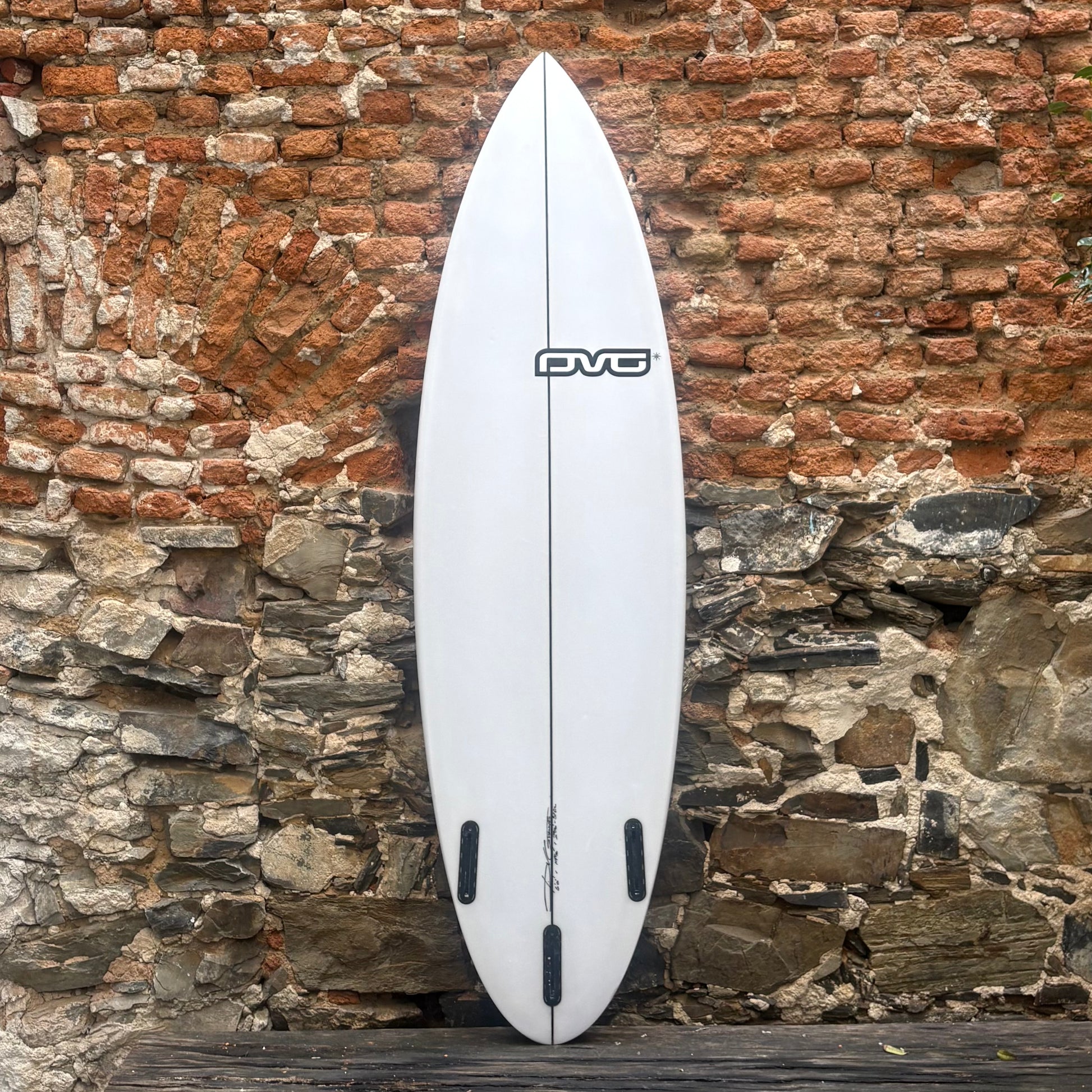 White surfboard with a logo against a rustic stone wall.