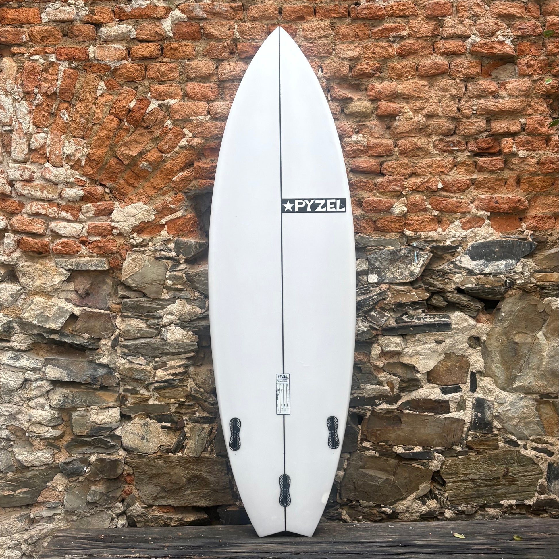 White surfboard with a visible brand logo against a stone wall.