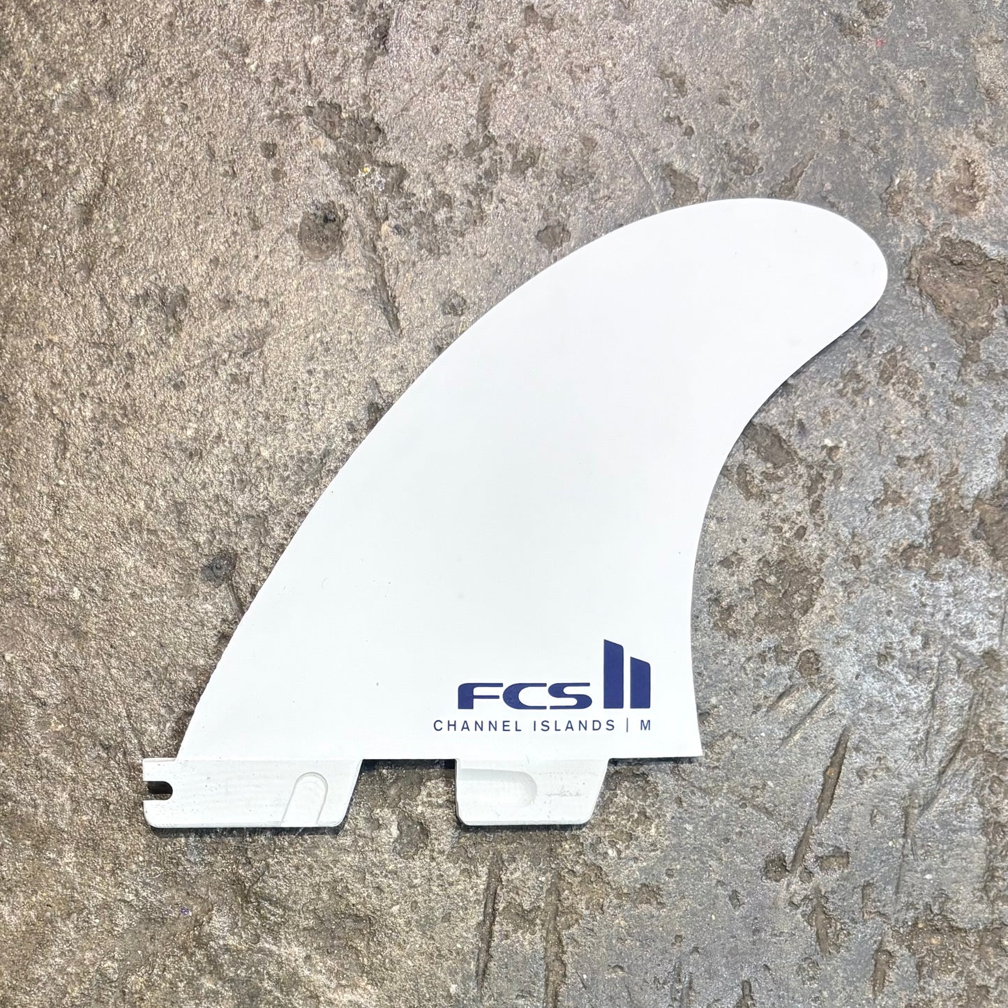 White surf fin with FCS logo on a textured surface