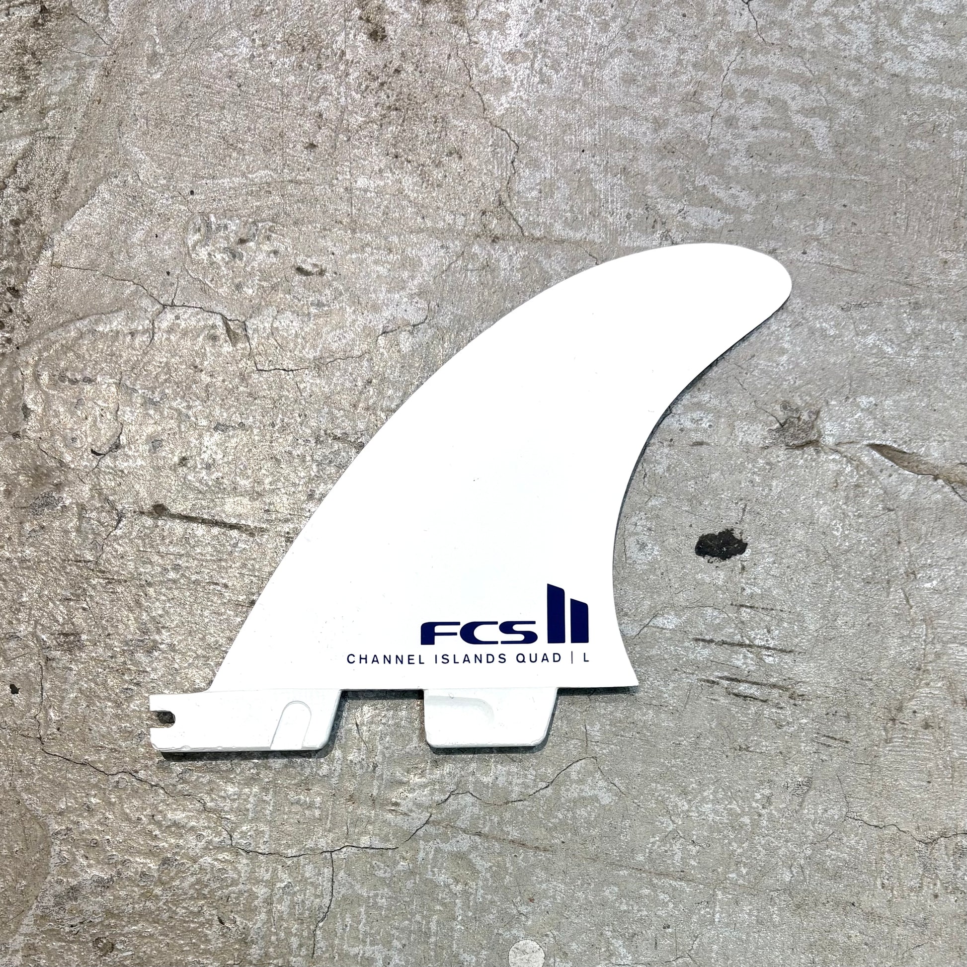 White surf fin with FCS logo on a textured gray surface
