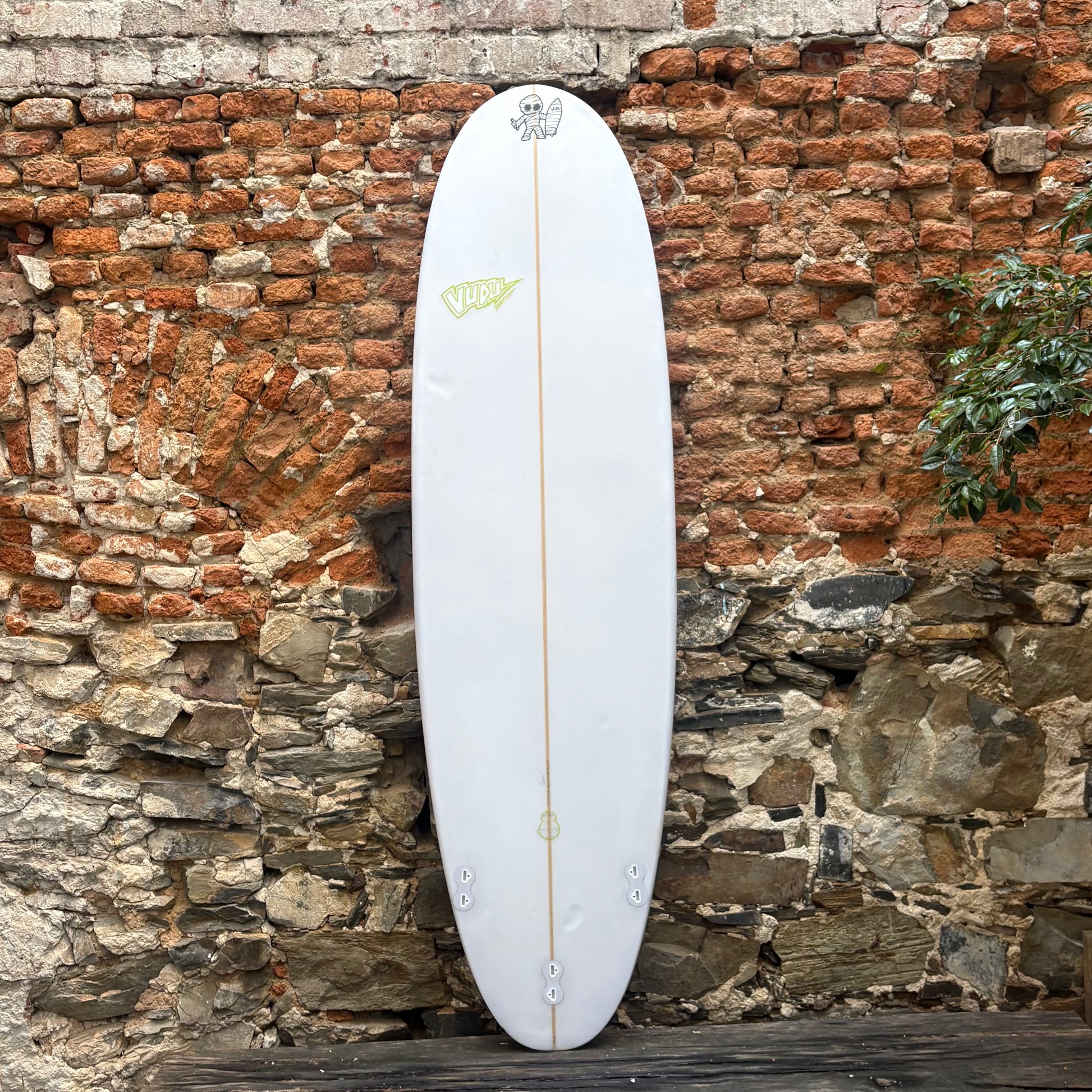 White surfboard with a logo against a rustic stone wall
