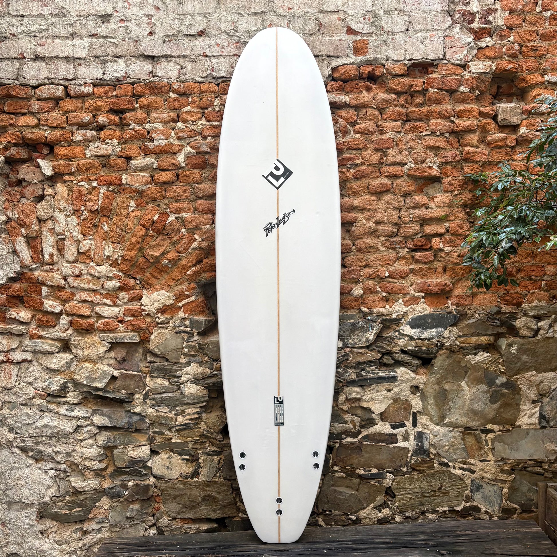 White surfboard with black logo against a rustic stone wall