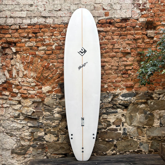 White surfboard with black logo against a rustic stone wall