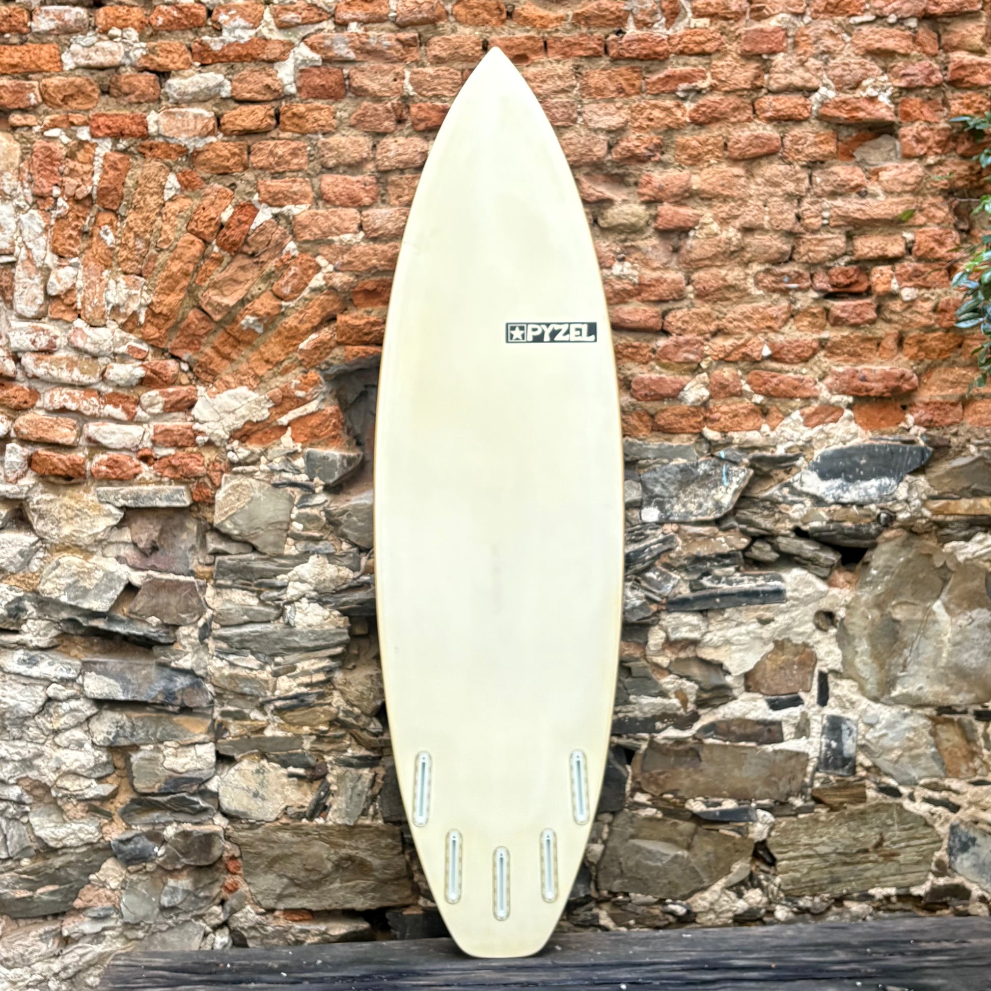 White surfboard leaning against a brick wall with stone foundation