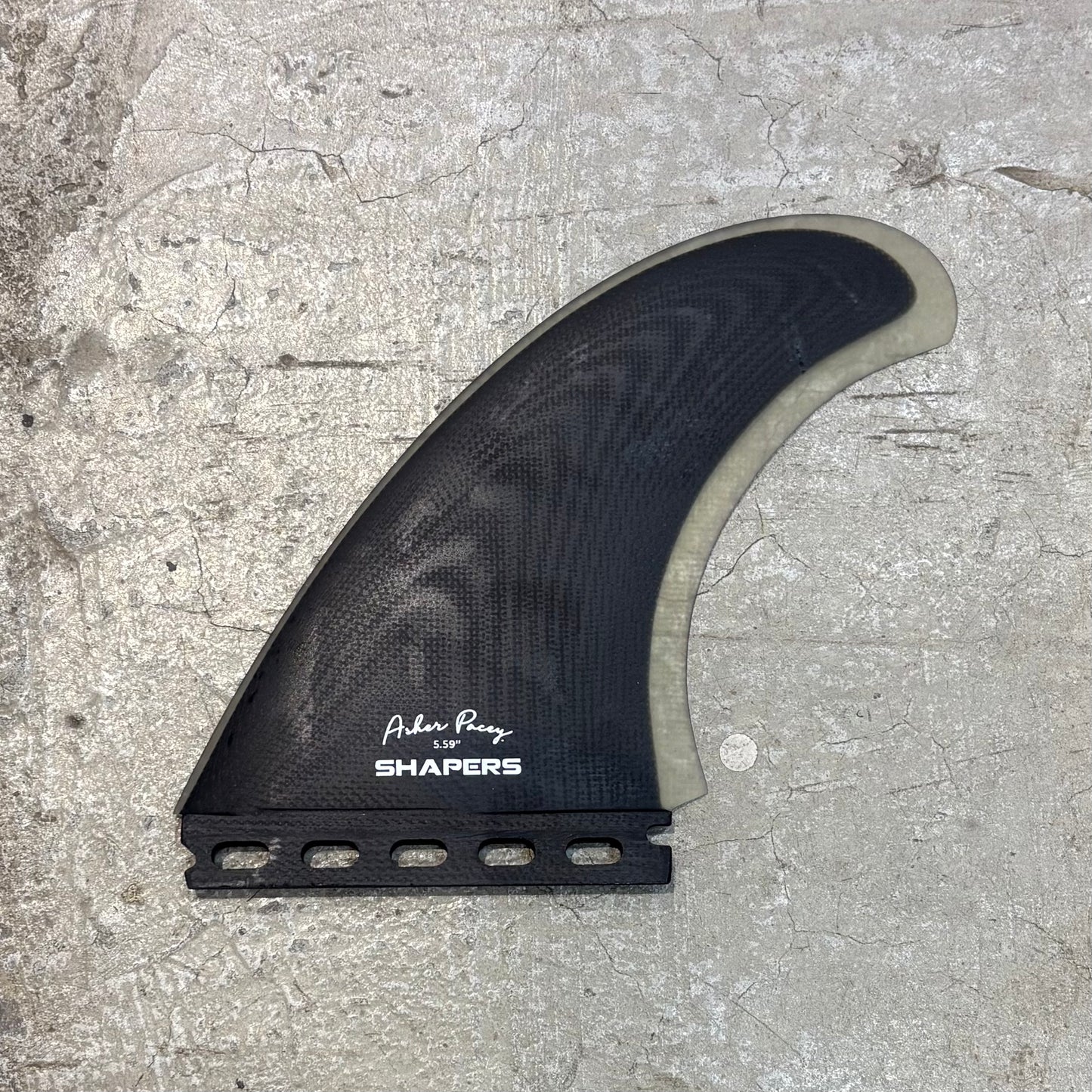 Surfboard fin with 'Shapers' branding on a concrete surface