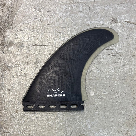 Surfboard fin with 'Shapers' branding on a concrete surface