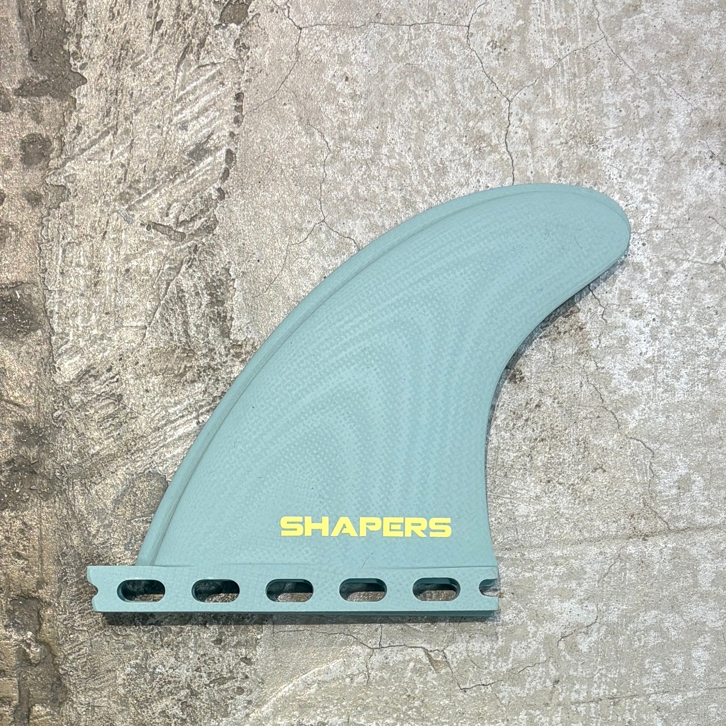 Surfboard fin with 'Shapers' branding on a textured surface