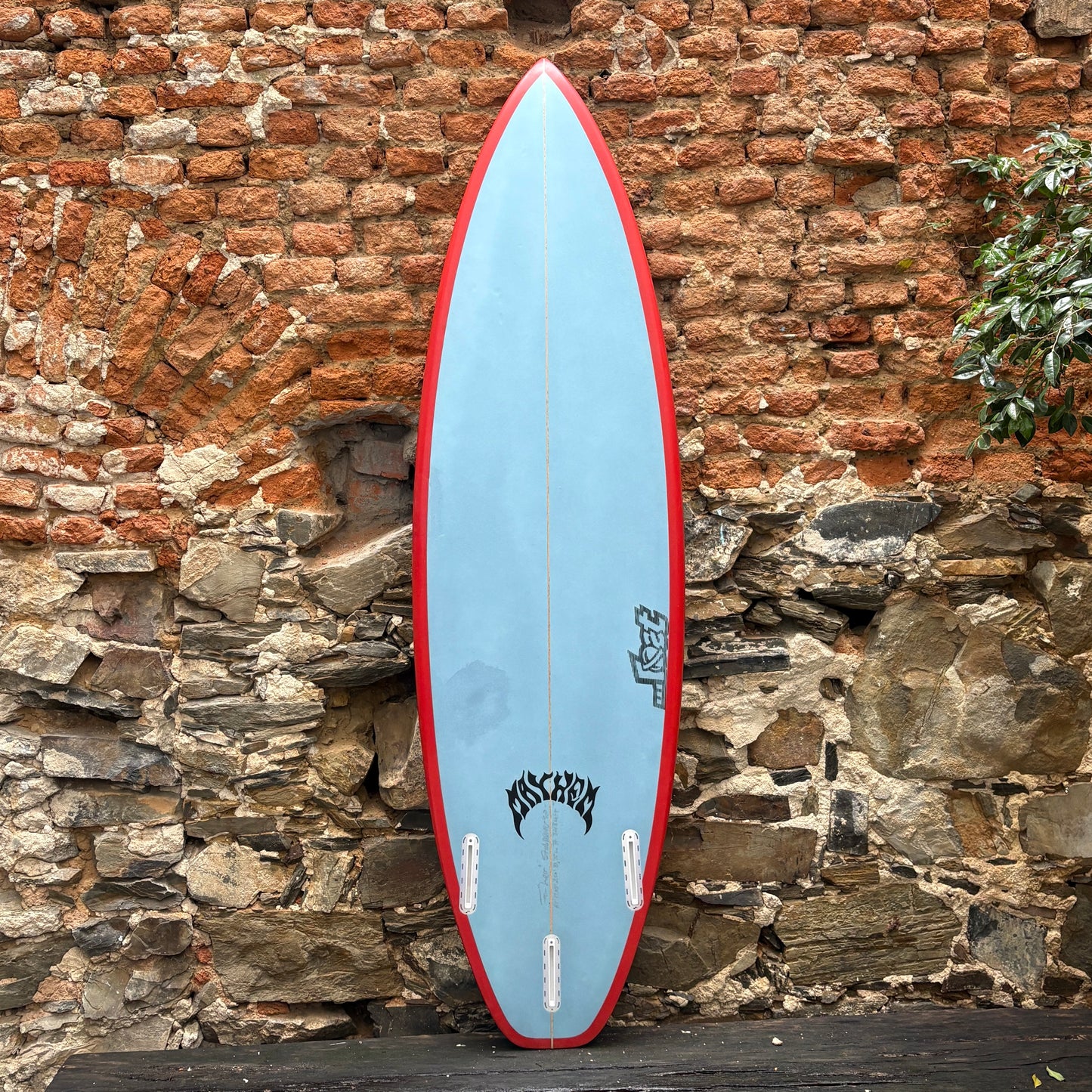 Blue and red surfboard leaning against a brick wall.