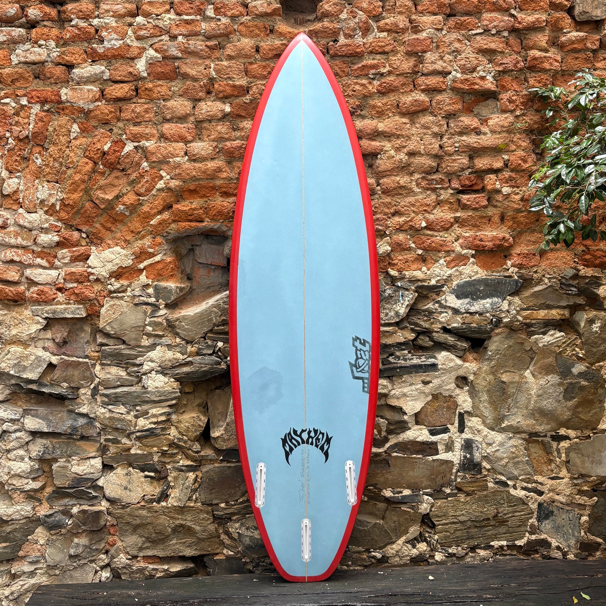 Blue and red surfboard leaning against a brick wall.