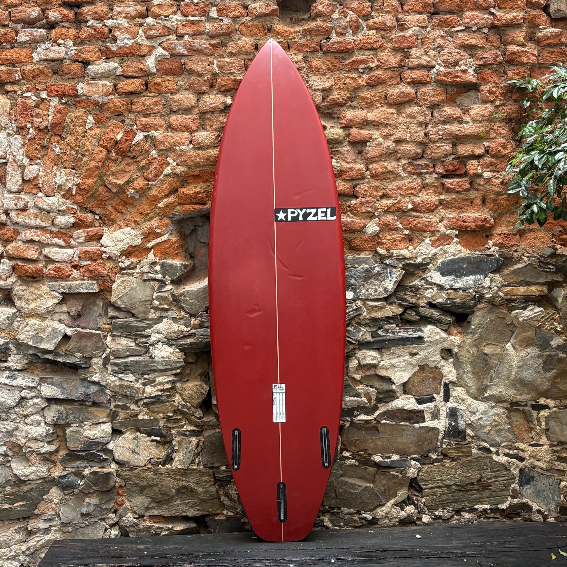Red surfboard with a visible brand logo leaning against a stone wall.