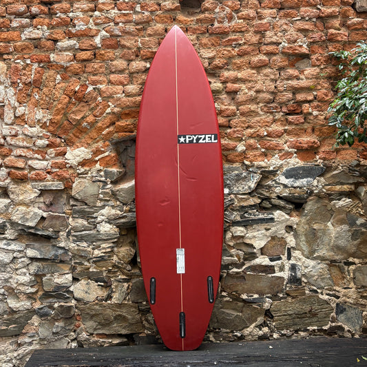 Red surfboard with a visible brand logo leaning against a stone wall.