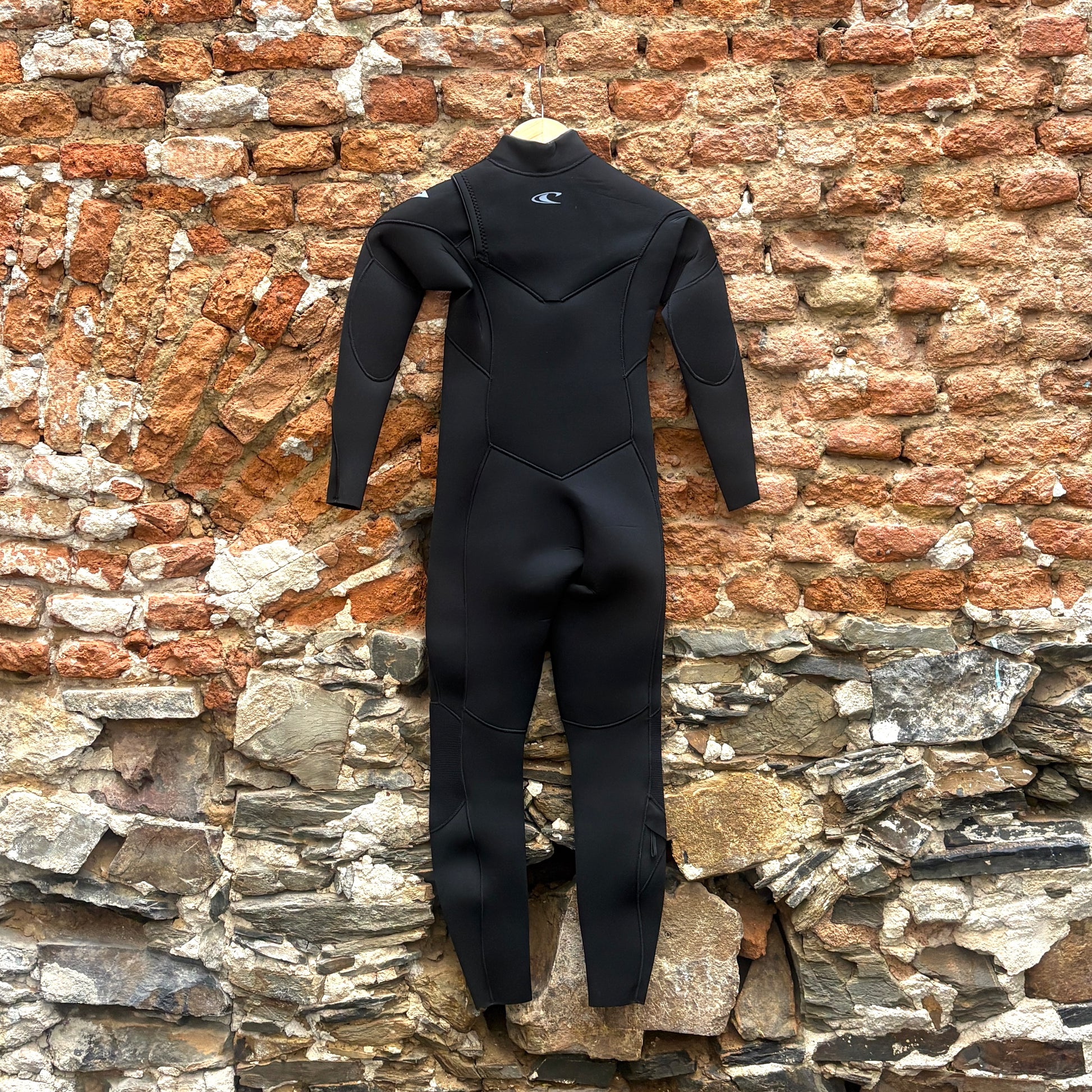 Back view of O'Neill Youth Epic 4/3mm+ Chest Zip - Black in front of a rustic stone wall