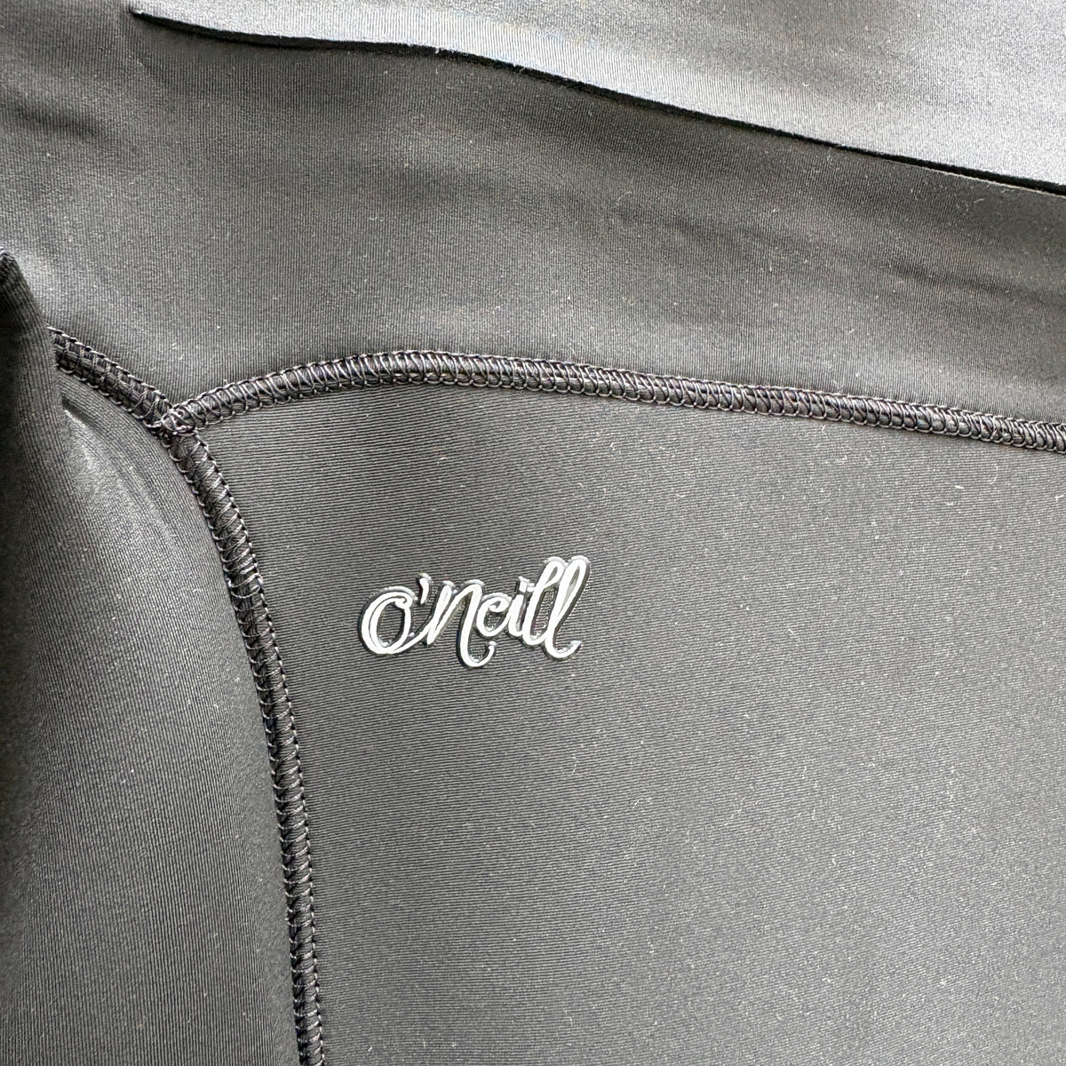 Close-up of a dark gray athletic garment with visible stitching and a small silver O'Neill logo on the chest.