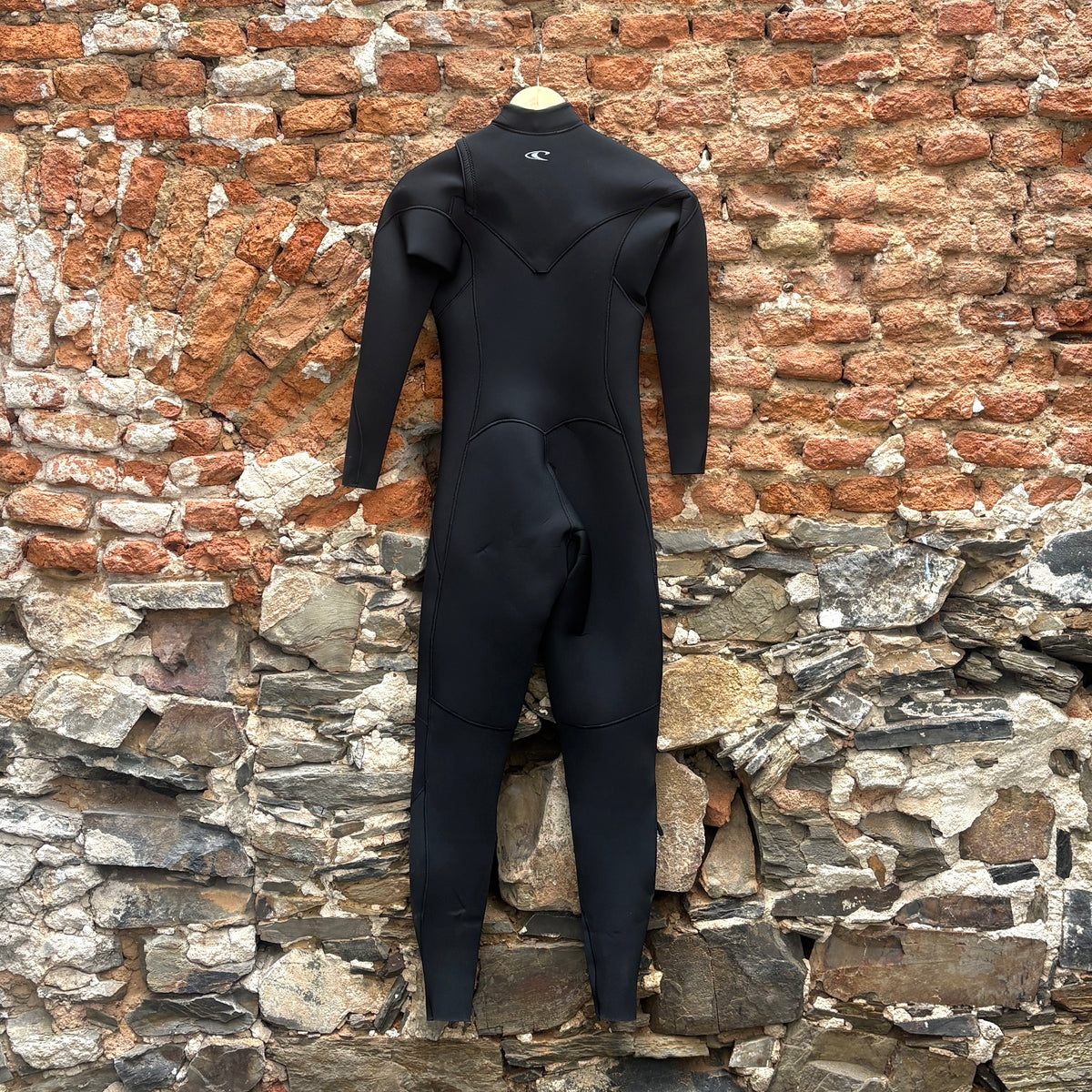 A black full-body wetsuit hangs from a wooden hanger against a rustic brick and stone wall background.