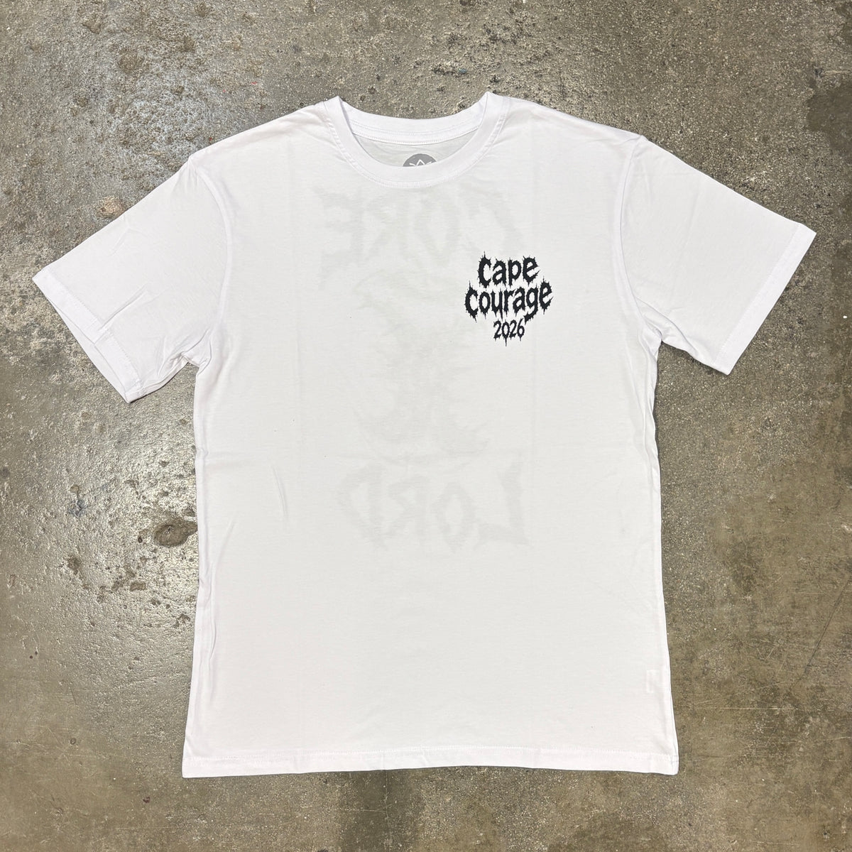A white short-sleeve crewneck t-shirt with a black graphic print on the left chest reading 'Cape Courage 2016', laid flat on a textured gray concrete surface.