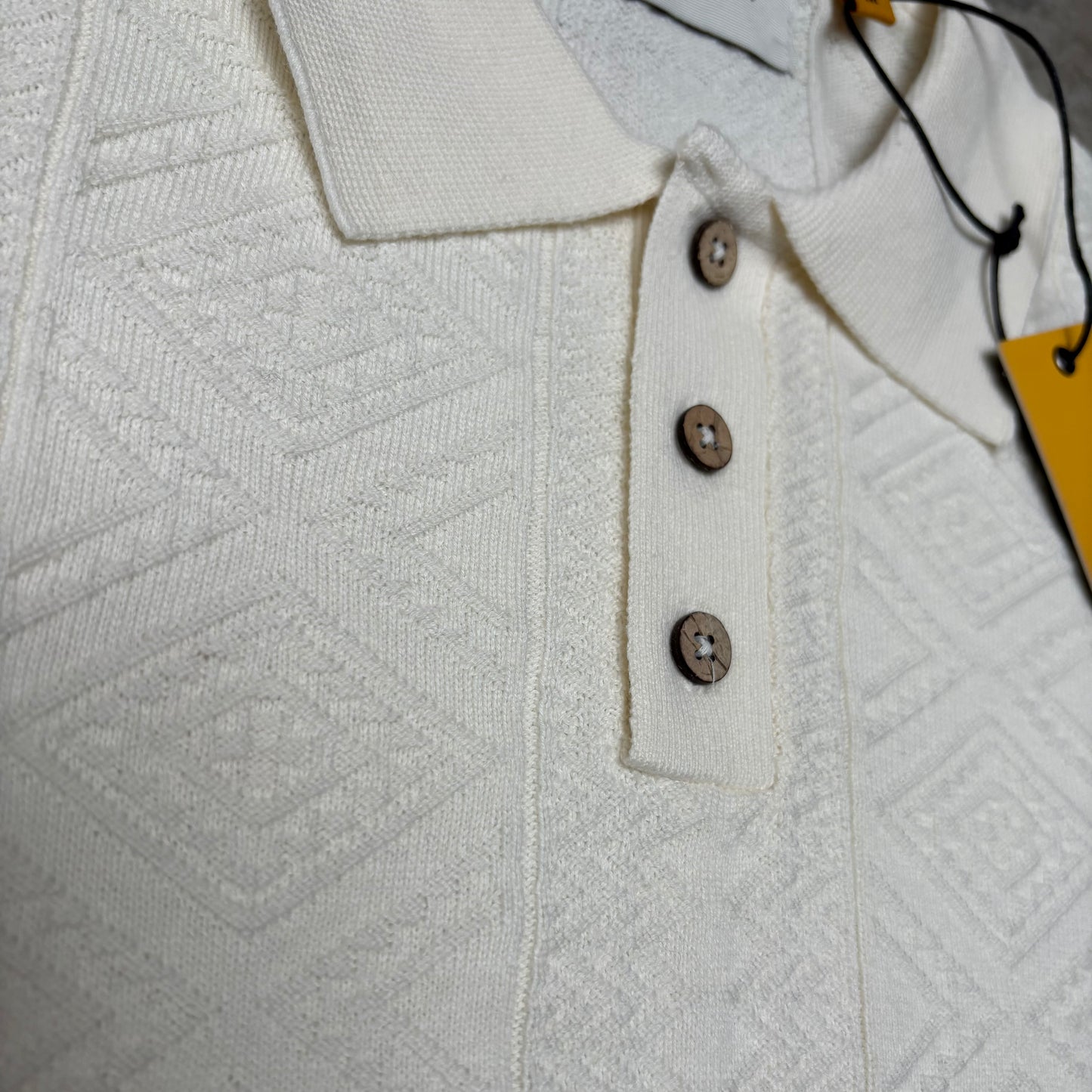 Close-up of a textured white shirt with buttons and a yellow tag.