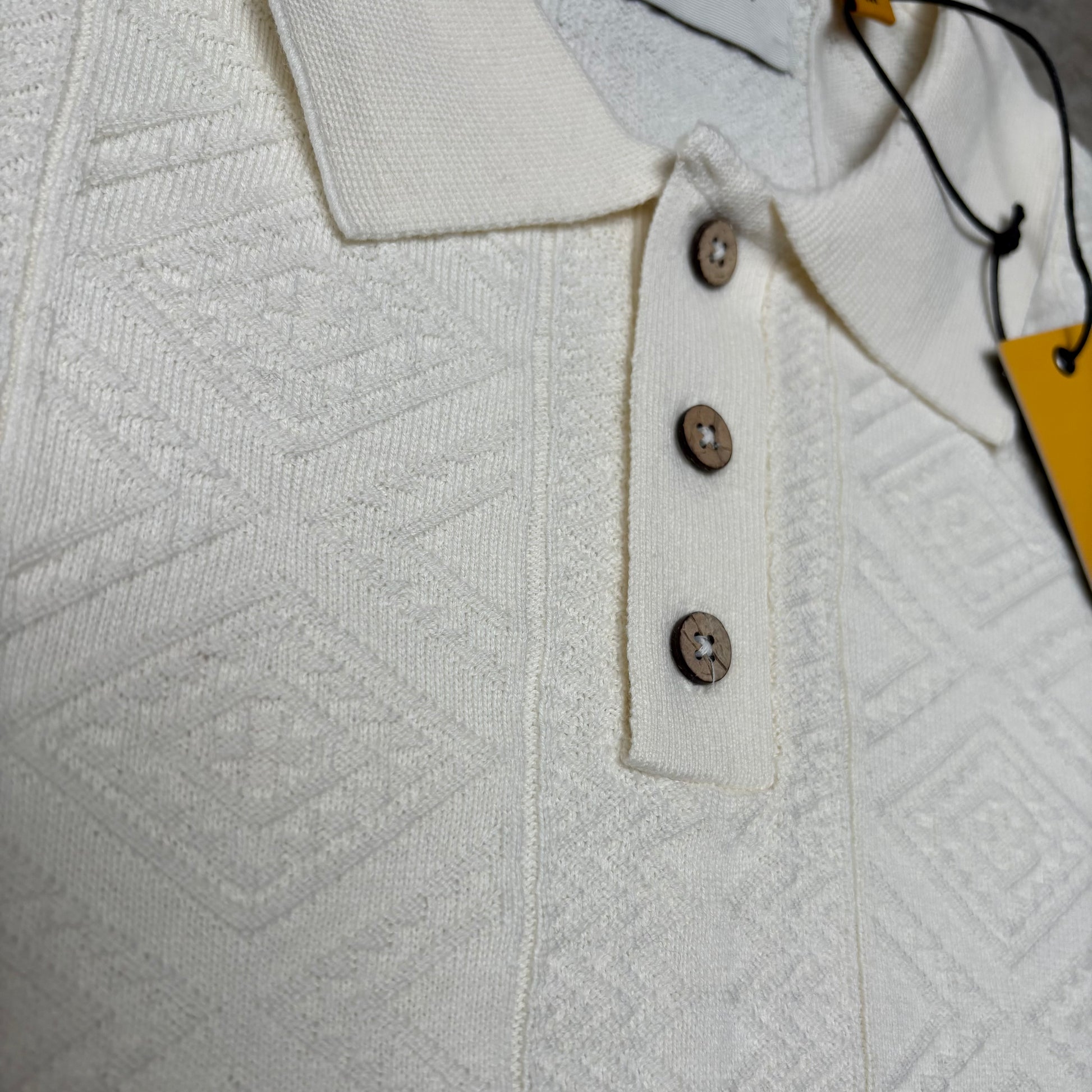 Close-up of a textured white shirt with buttons and a yellow tag.