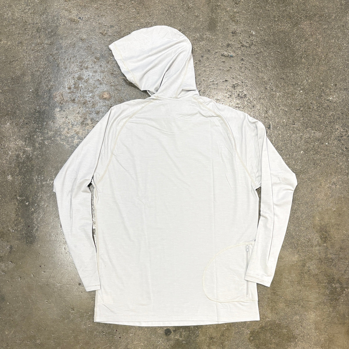A white hooded long-sleeve shirt laid flat on a textured concrete floor, viewed from the back.