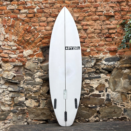 A white Pyzel surfboard standing upright against a rustic brick and stone wall.