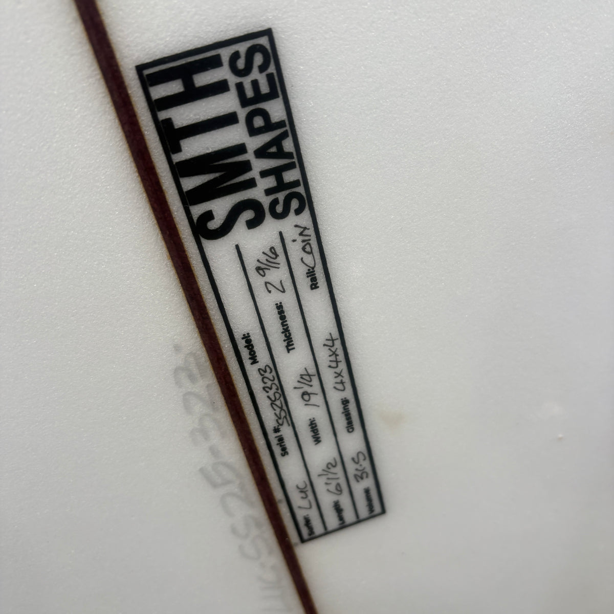 A close-up of a white textured surface with a black rectangular label reading 'SMITH SHAPES' and handwritten product details, alongside a dark brown vertical line.