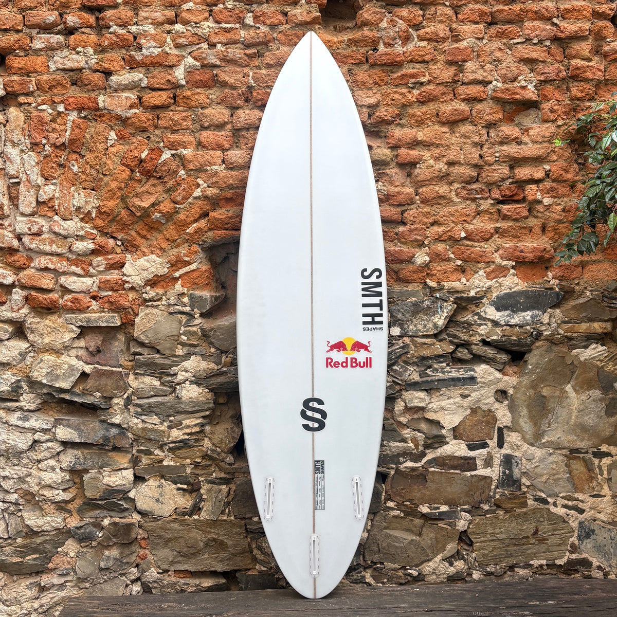 Back view of a white SMTH Shapes Volume Surfboard against a rustic wall