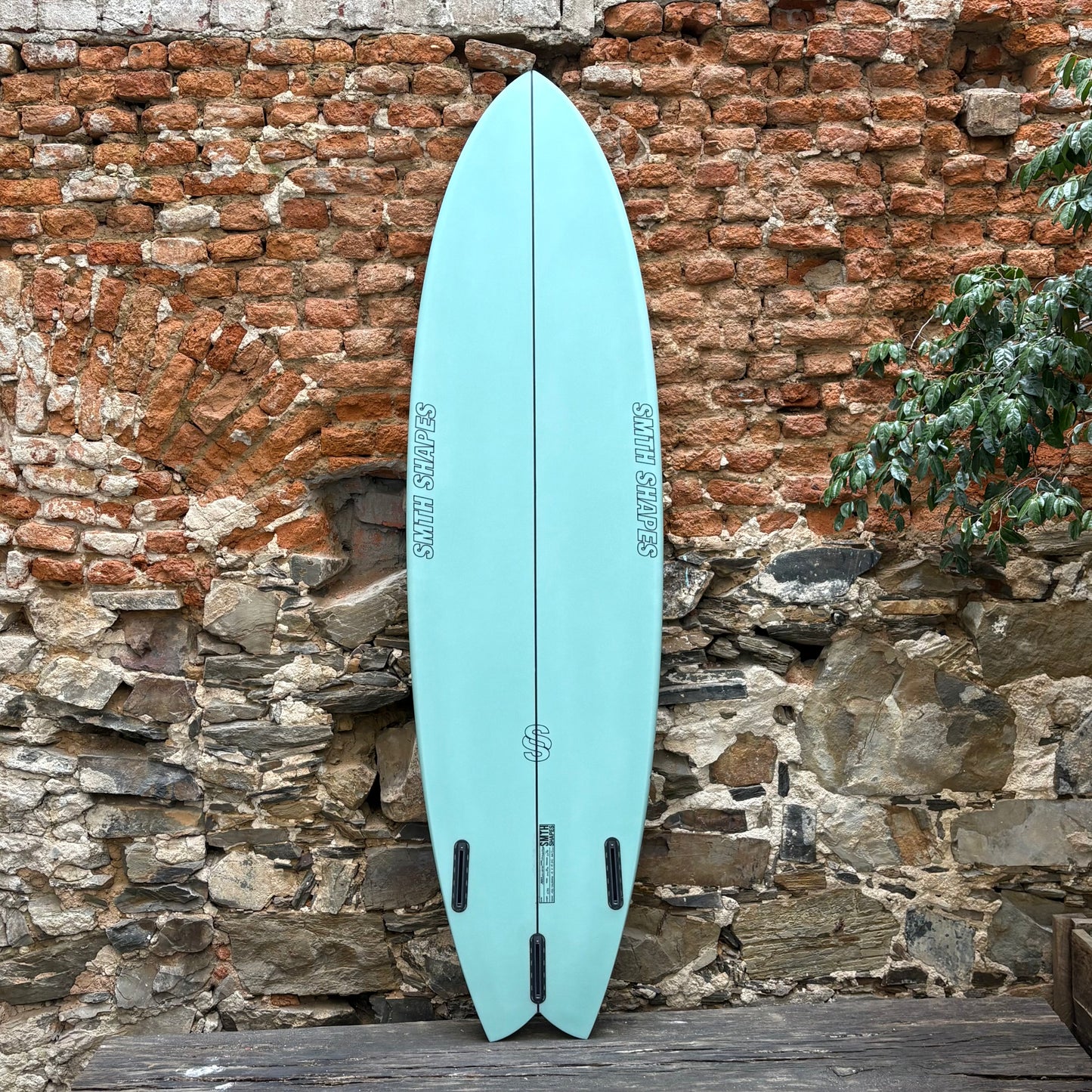 Light blue surfboard leaning against a rustic stone wall.