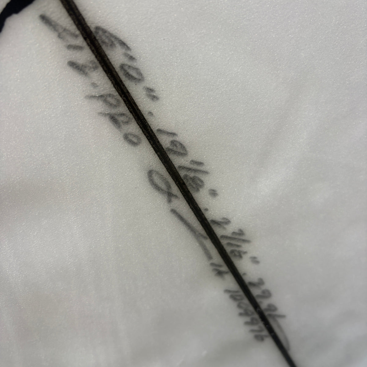 A close-up of a black writing on white on a surfboard, featuring cursive script text running diagonally across the surface.