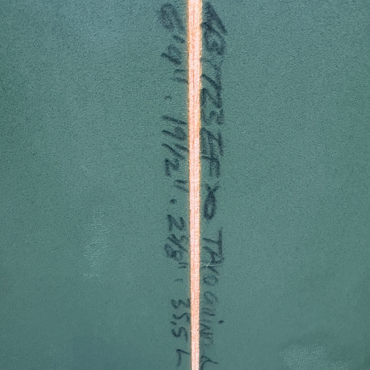 A close-up of a teal-green textured surface with a vertical beige stripe running down the center and dark handwritten markings near the right side.