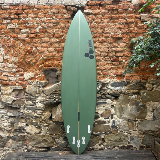 A green surfboard with black and white graphics, standing upright against a rustic brick and stone wall.