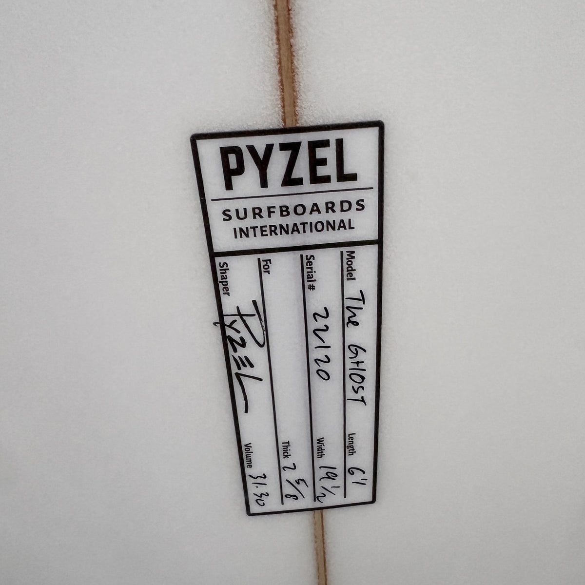 A close-up of a white Pyzel Surfboards International sticker on a white surfboard, showing handwritten details for 'The Ghost' size 6.1.