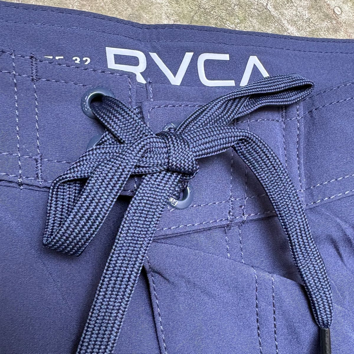 Close-up of a pair of navy blue shorts with a matching woven drawstring tied in a bow. The brand name 'RVCA' is printed in white on the waistband.