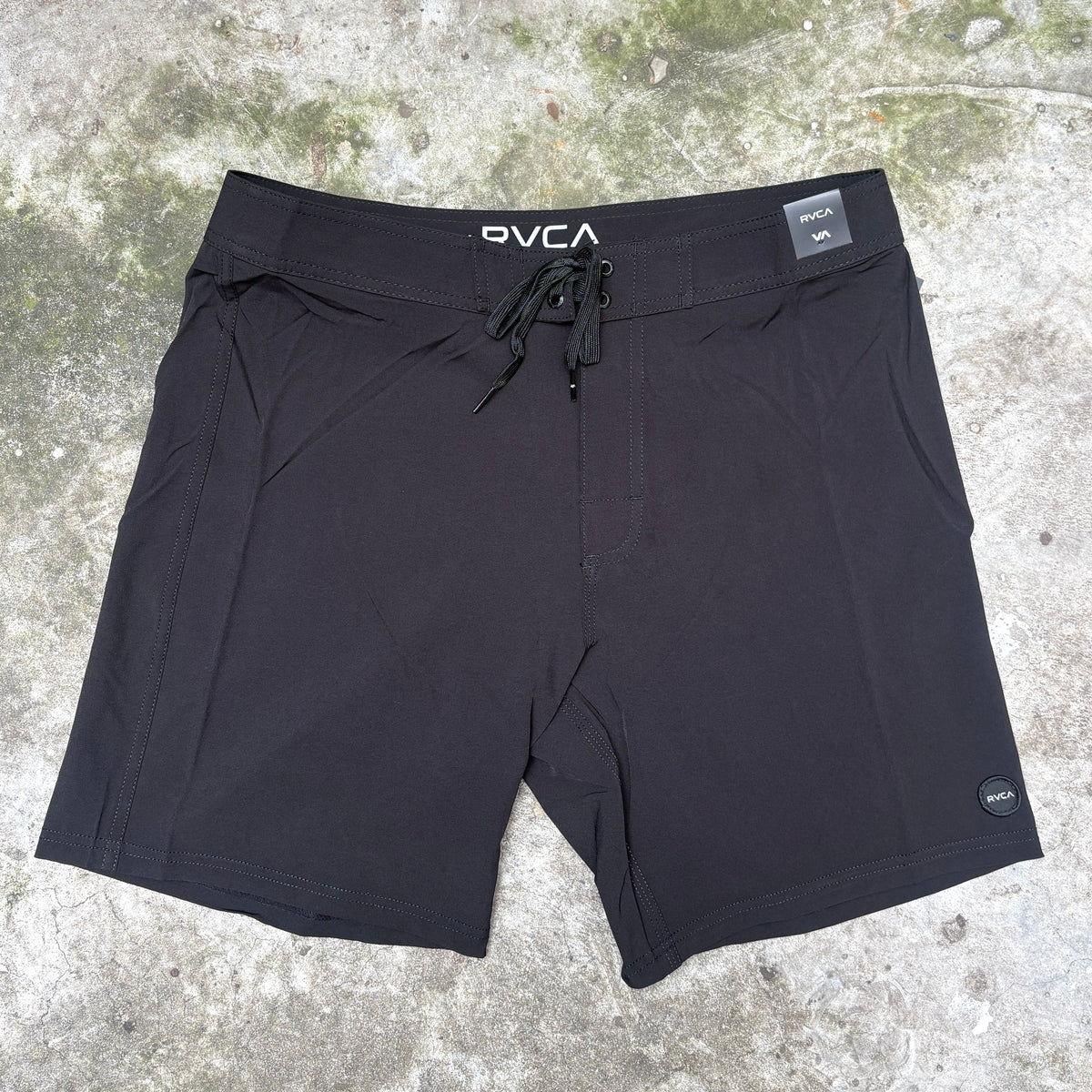 Black OVCA athletic shorts with a drawstring waist, laid flat on a textured concrete surface.