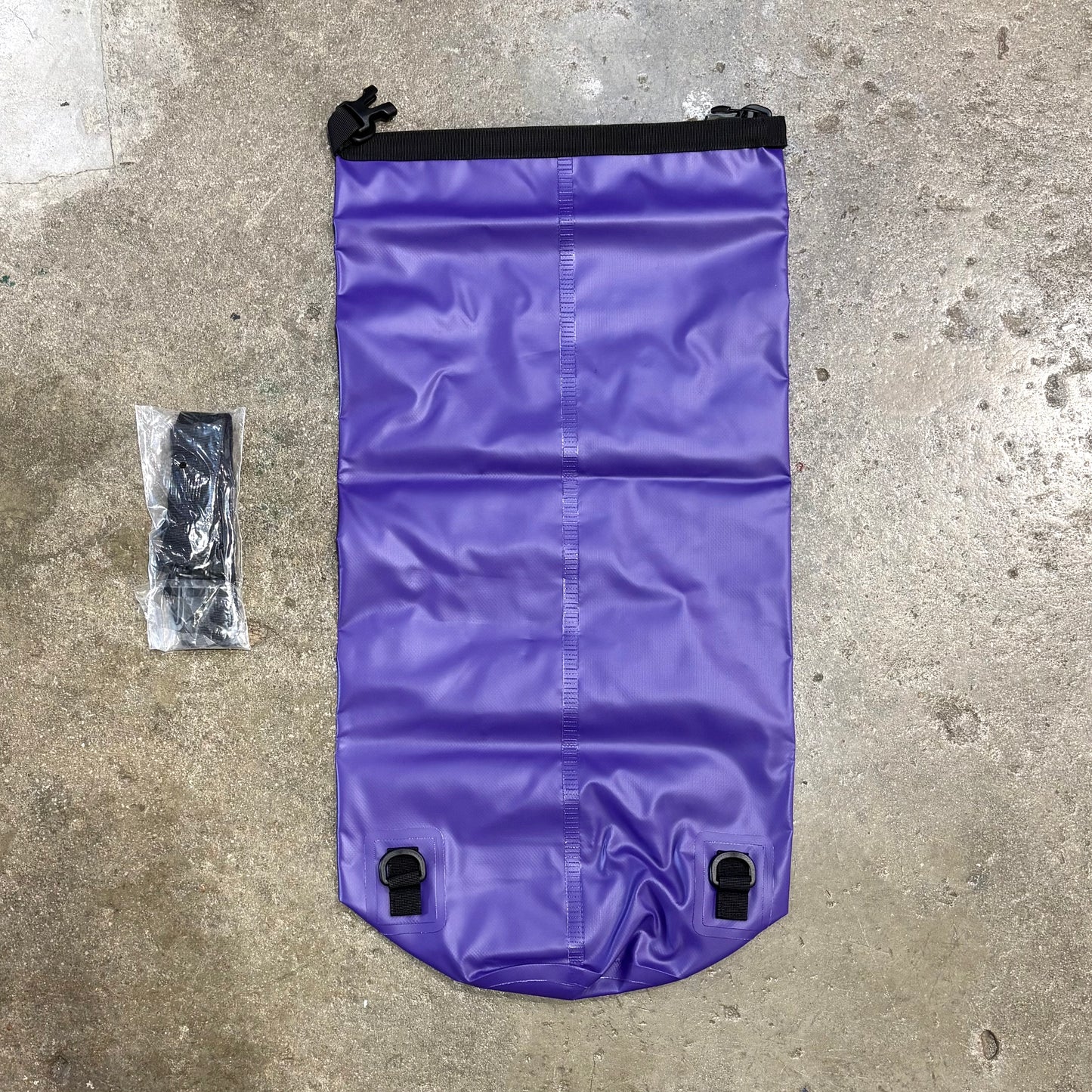 Purple waterproof bag with black zippers on a concrete surface