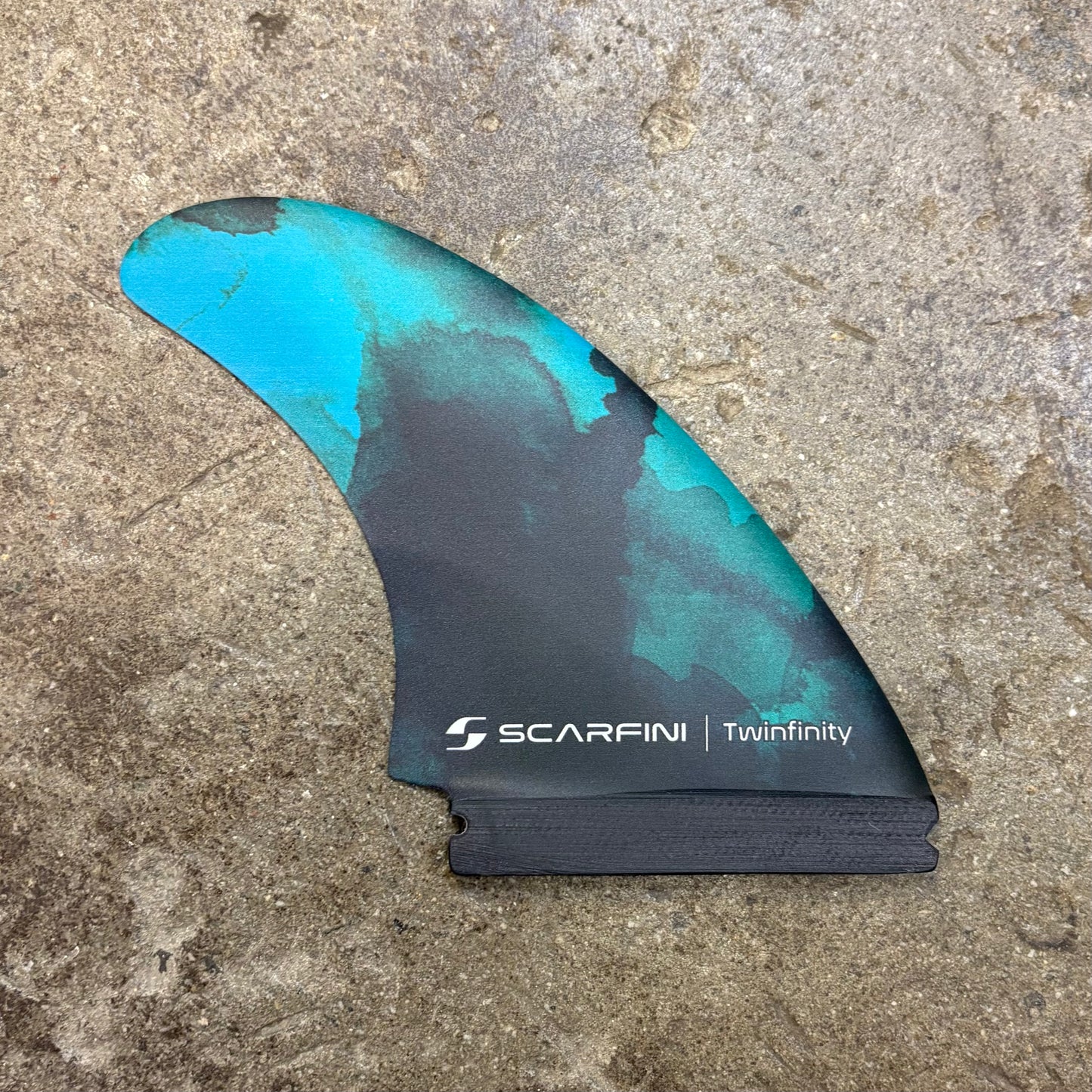 Blue and black surf fin with Scarfini Twinfinity logo on a concrete surface