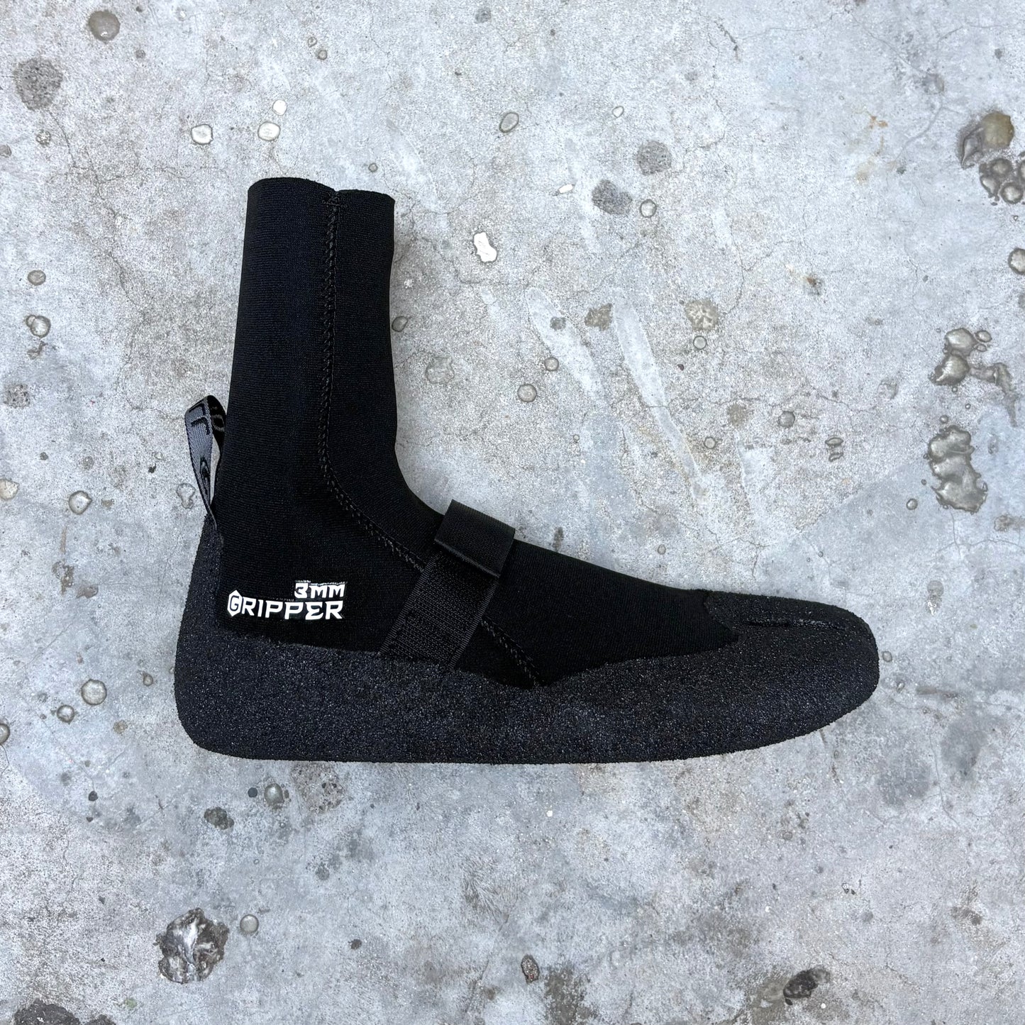 Black neoprene boot with '3mm Ripper' label on a concrete surface