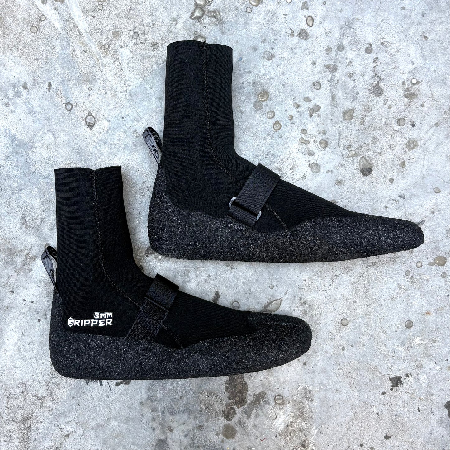 Pair of black neoprene boots with buckles on a textured concrete surface