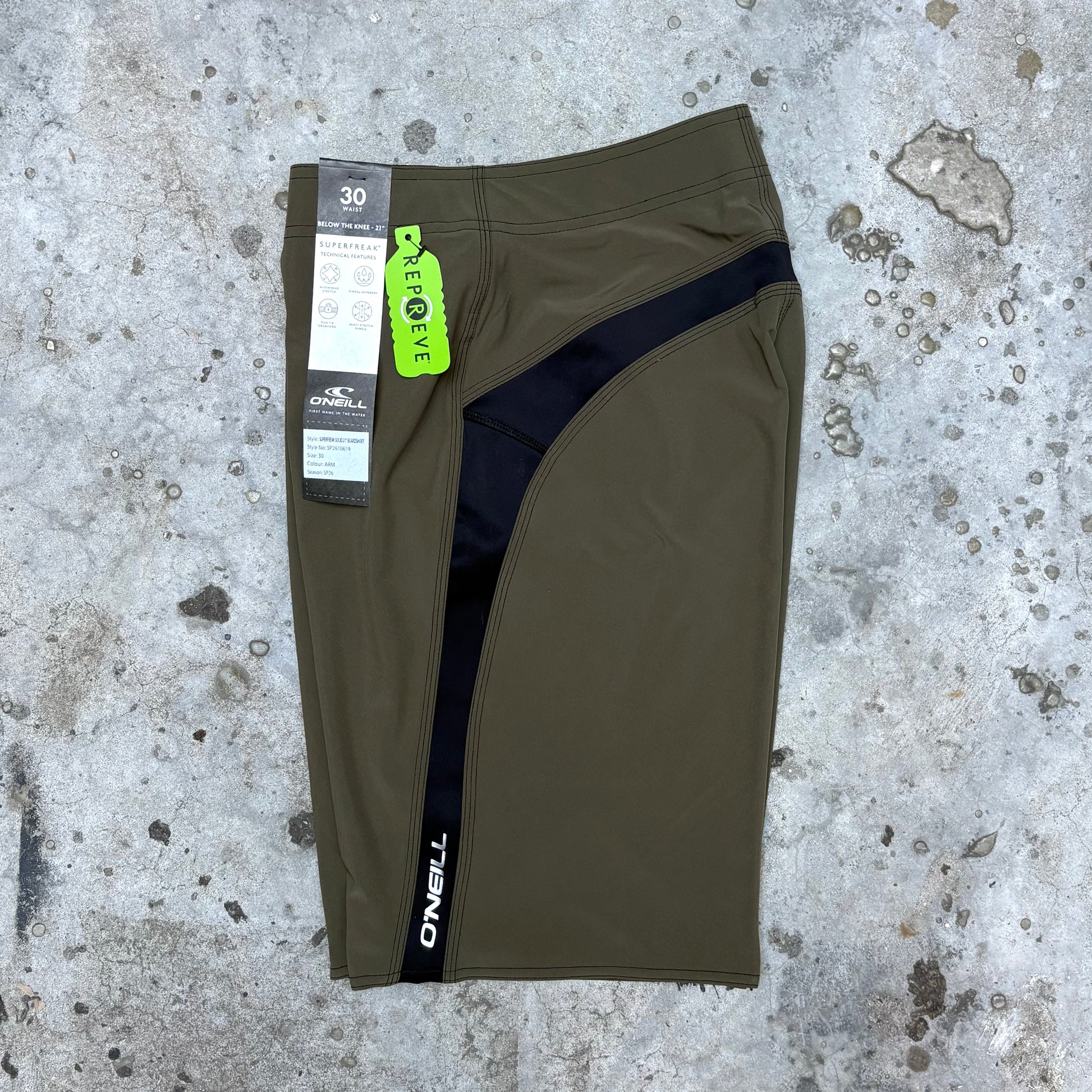 Green athletic shorts with a brand tag on a textured concrete surface