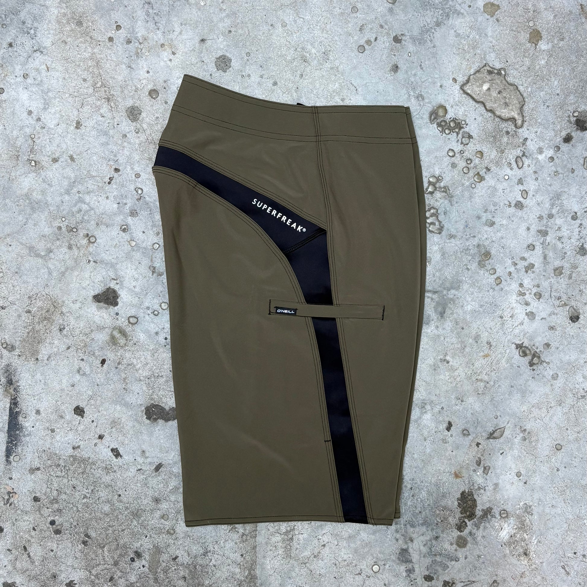 Khaki shorts with a black stripe on a textured concrete surface