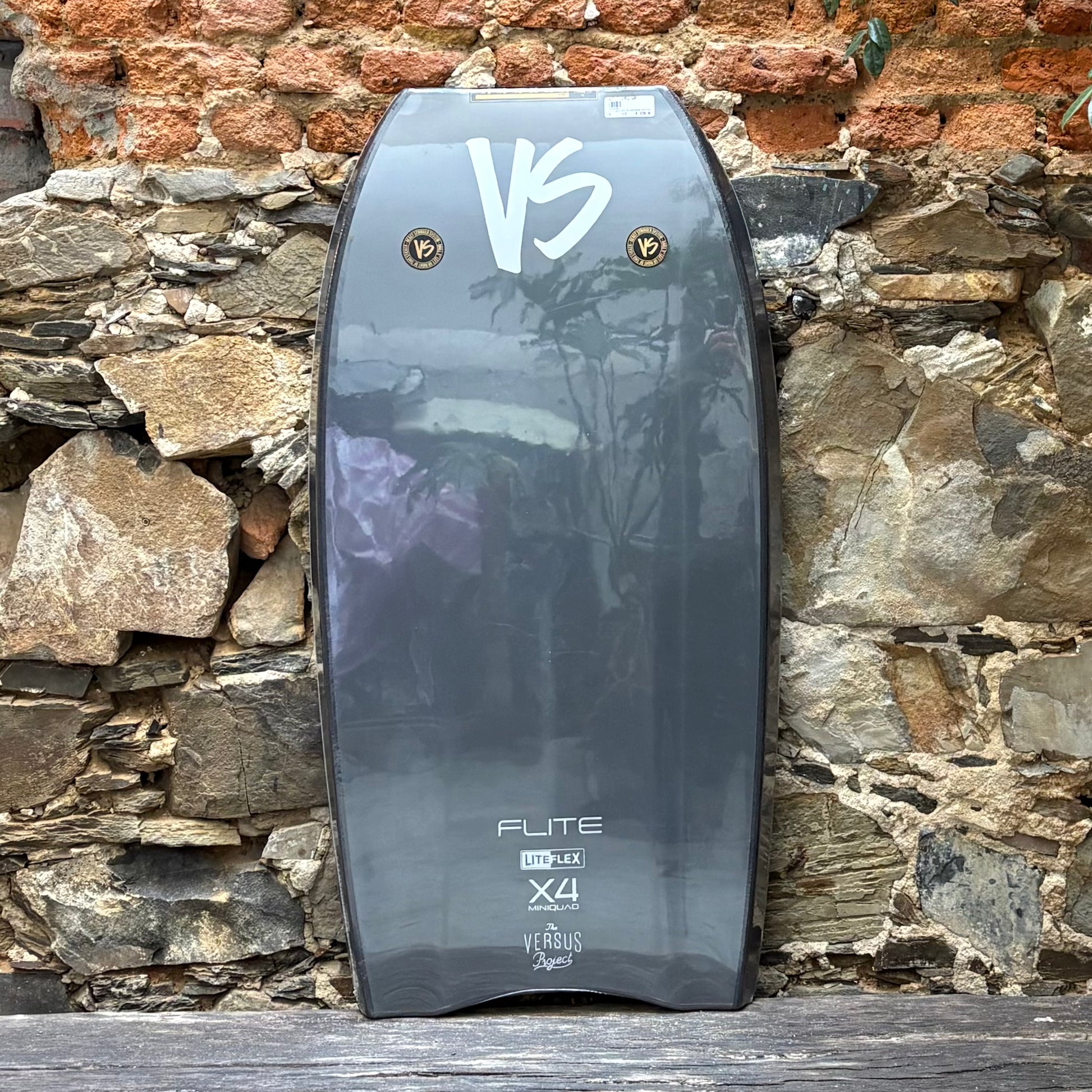 Bodyboard with 'VS' branding against a stone wall