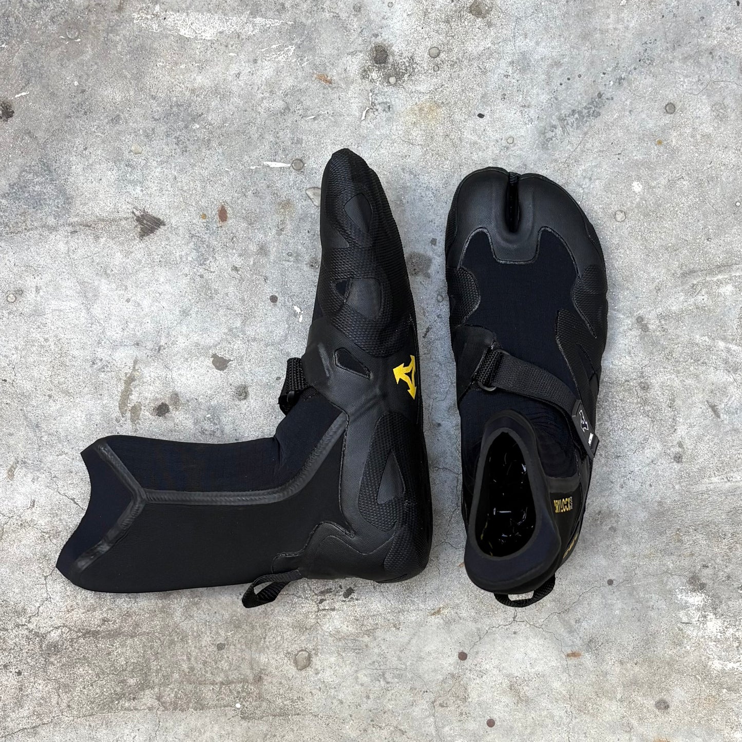 Black surf boots shoes with a yellow logo on a concrete surface