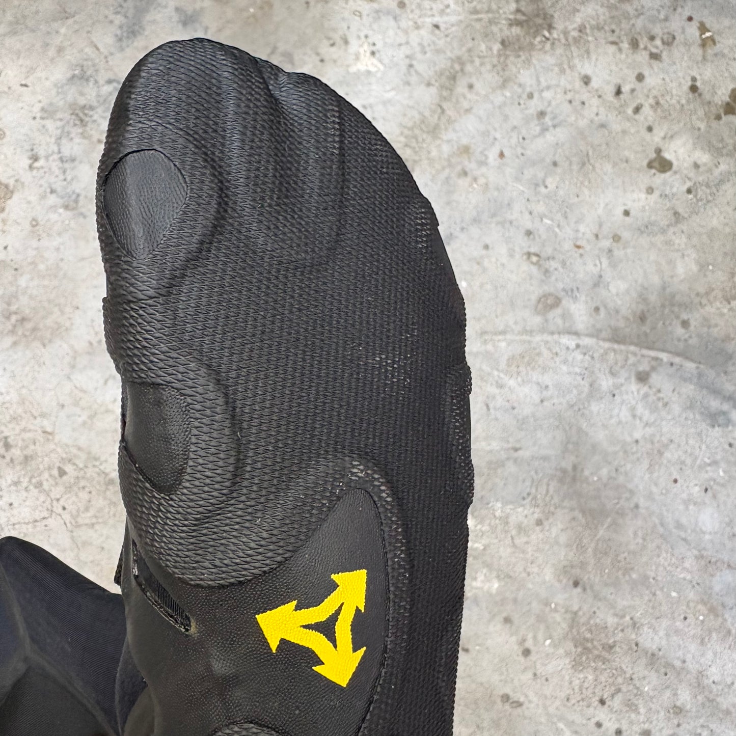 Black surfing boot with a yellow logo on a concrete floor