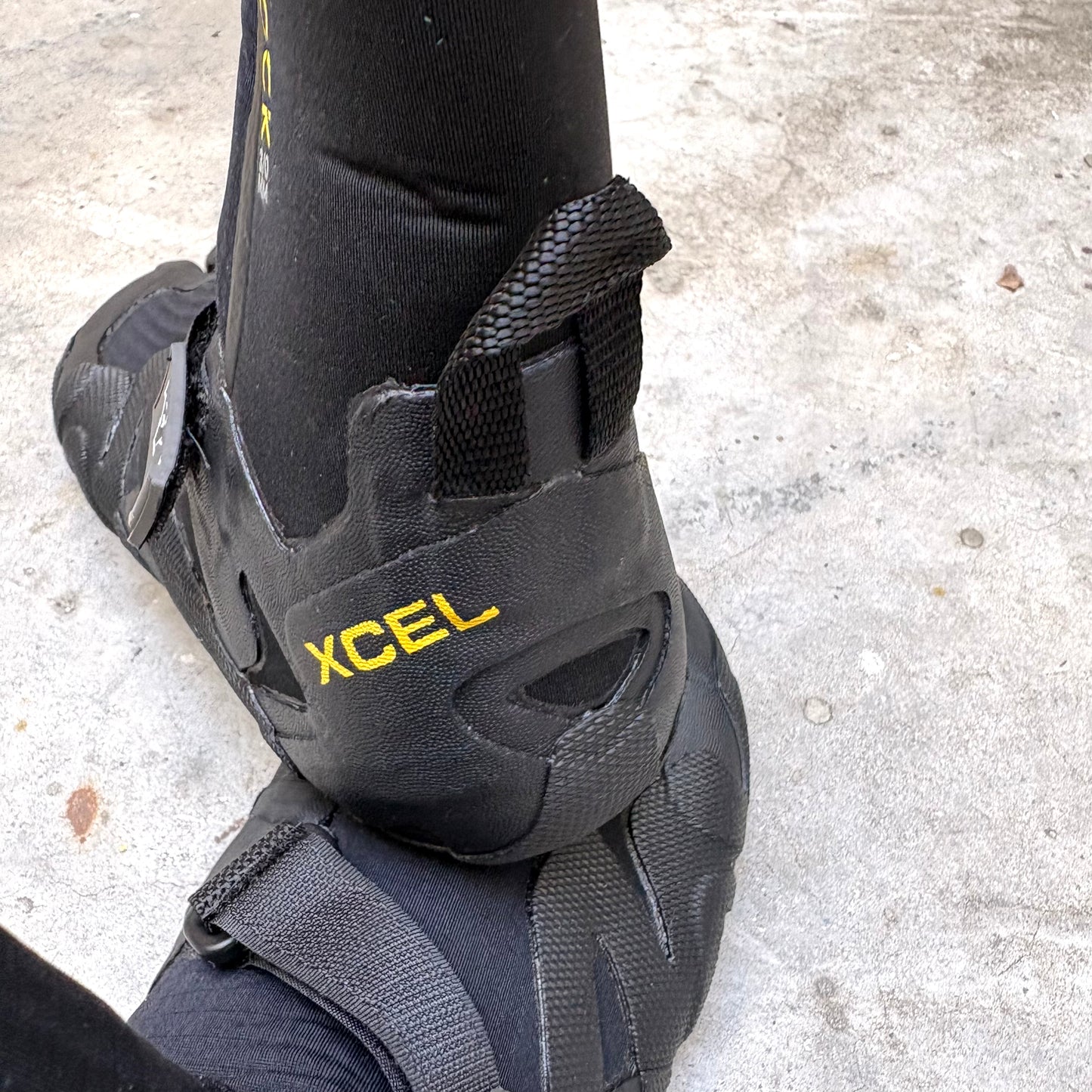 Black wetsuit boot with XCEL branding on a concrete surface