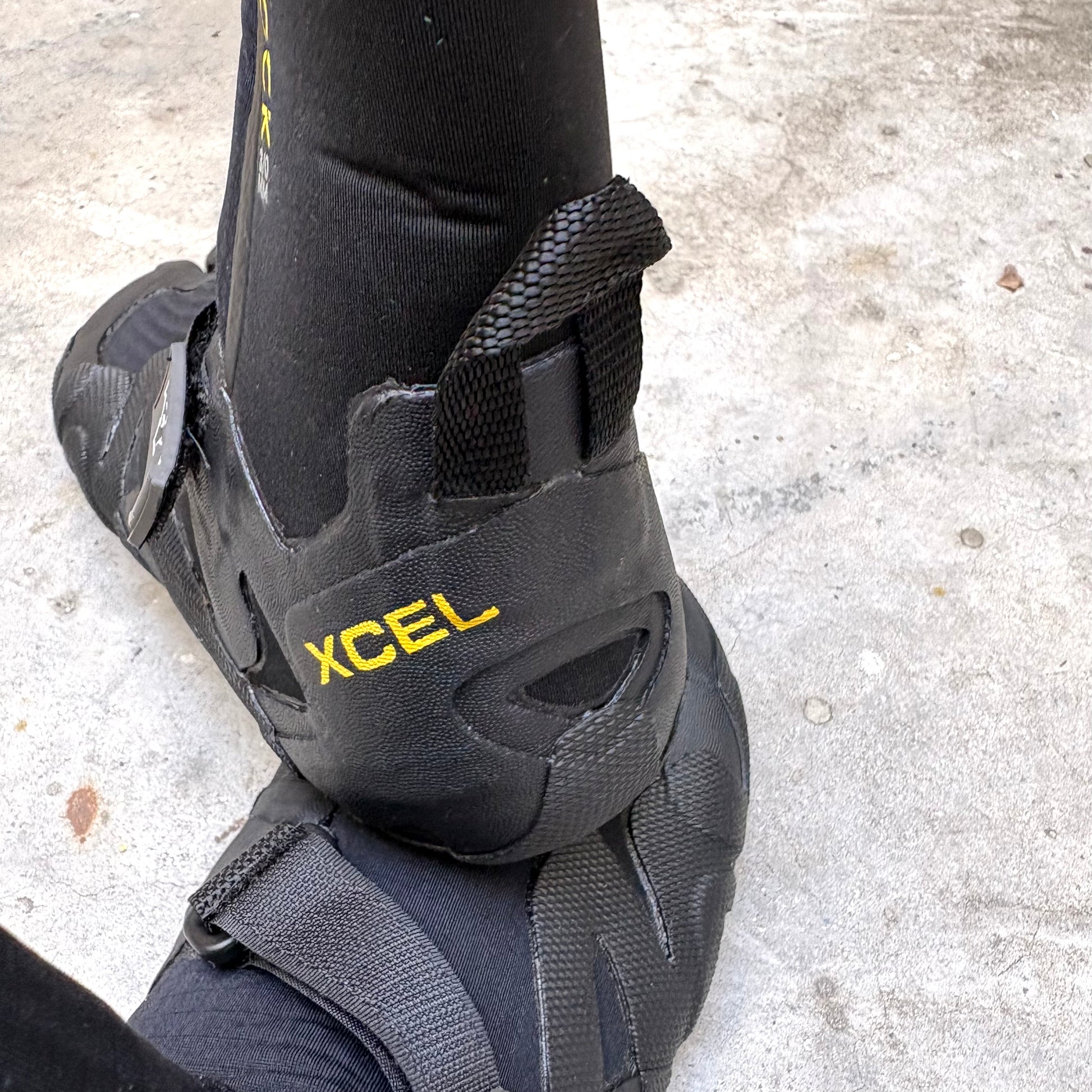Black wetsuit boot with XCEL branding on a concrete surface