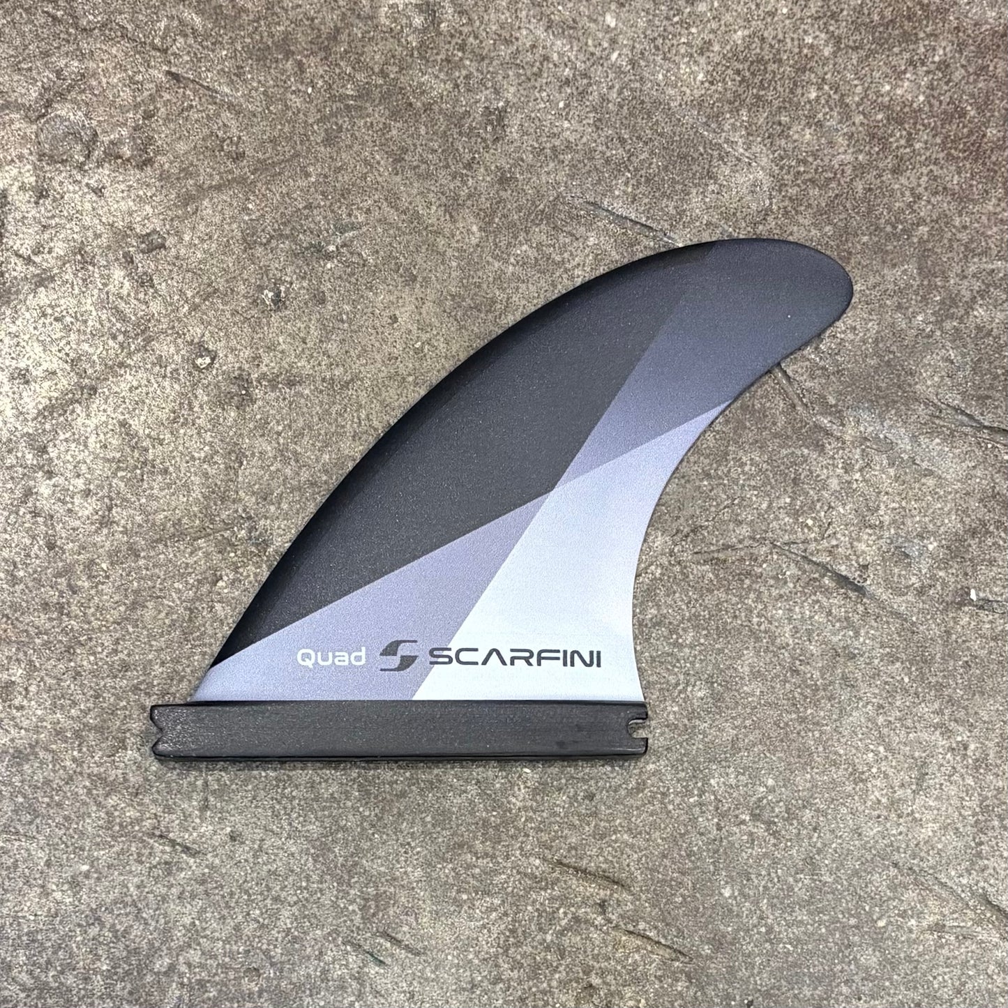 Surfboard fin with Scarfing branding on a concrete surface